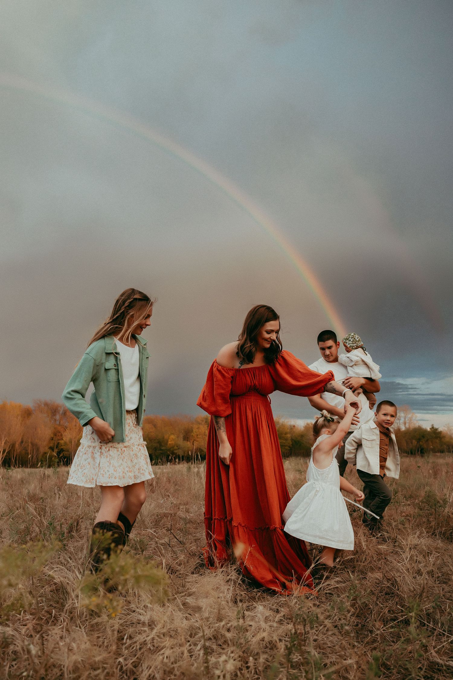 Family playing in field with rainbow visible in cloudy sky.