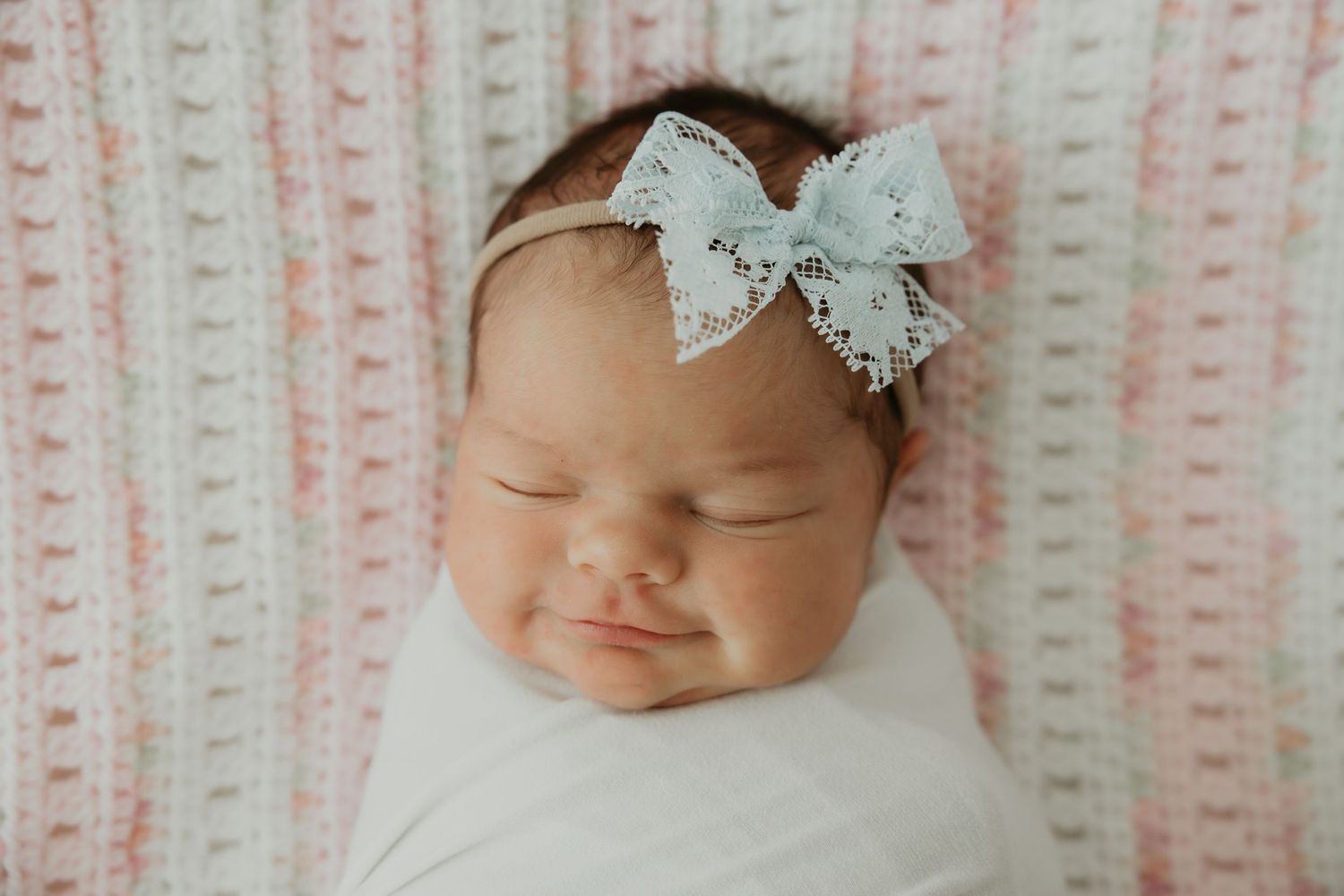 Sleeping baby wearing delicate lace bow on striped pink background.