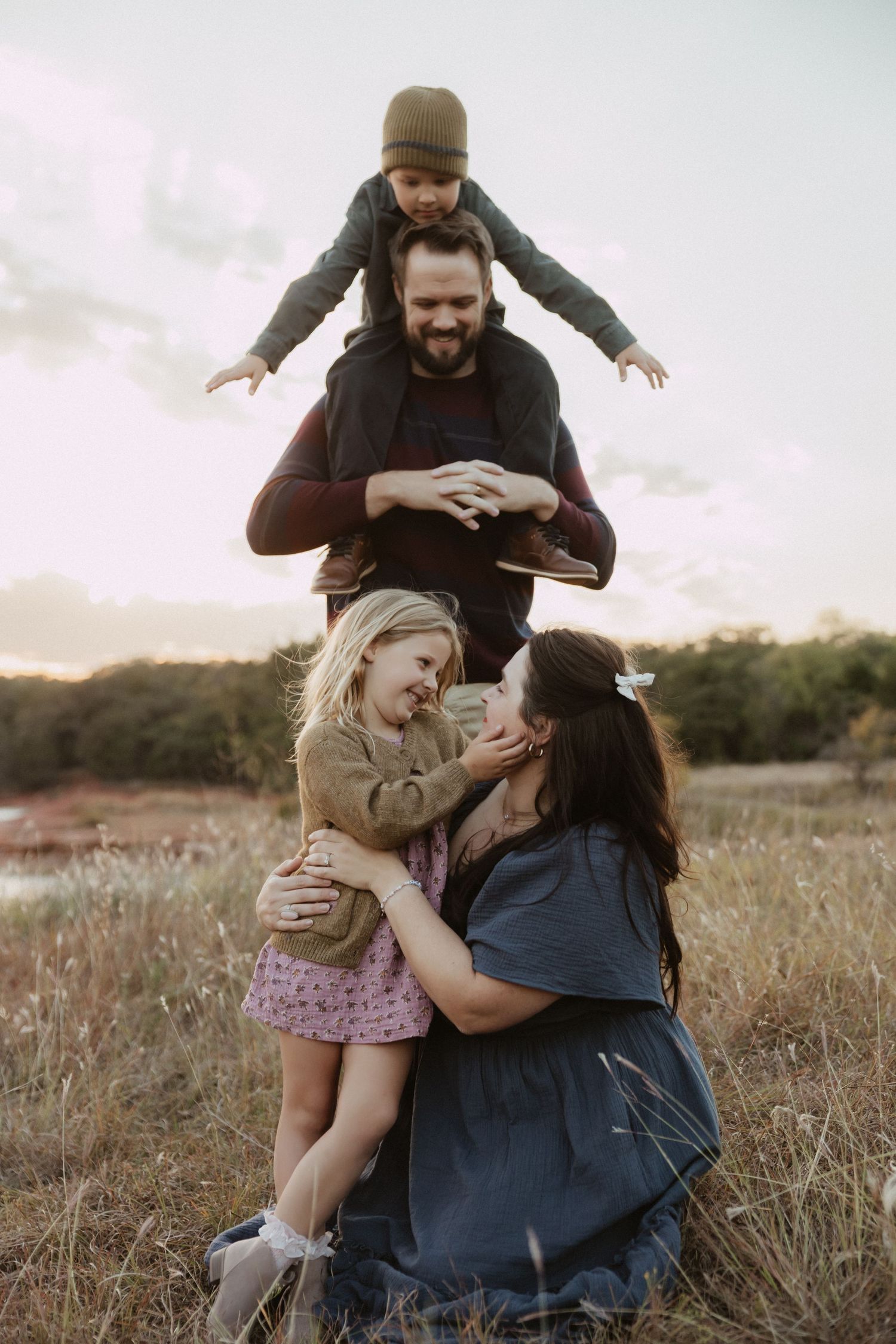 Family shares joyful moments together in rustic field during sunset.