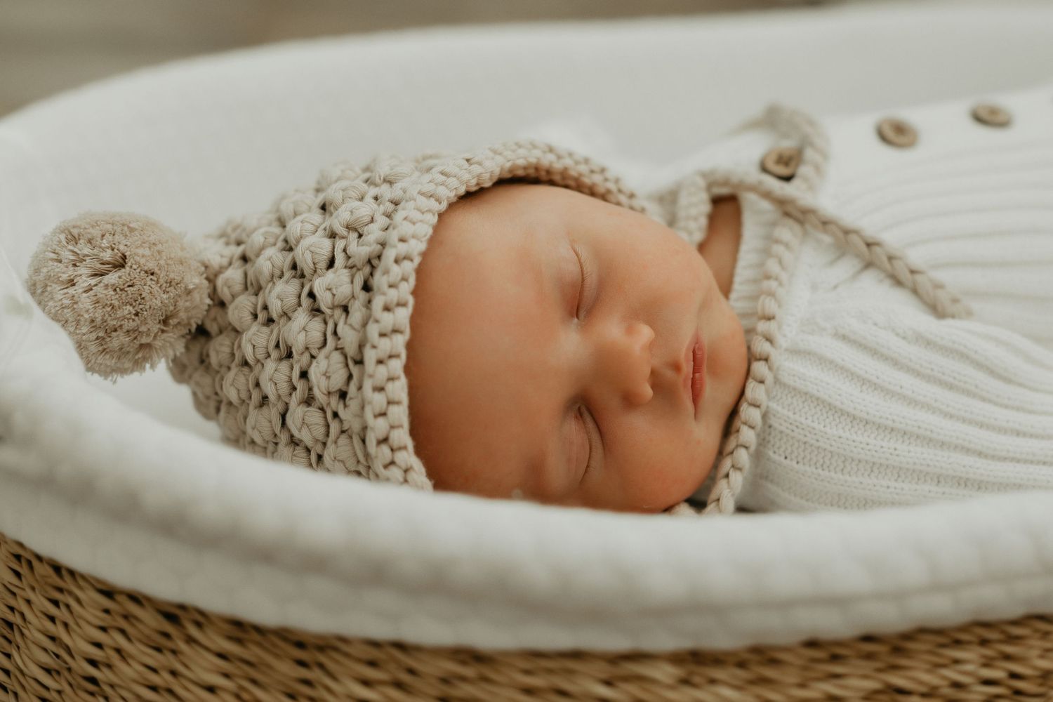 Peaceful sleeping baby in white bassinet with knitted bonnet.