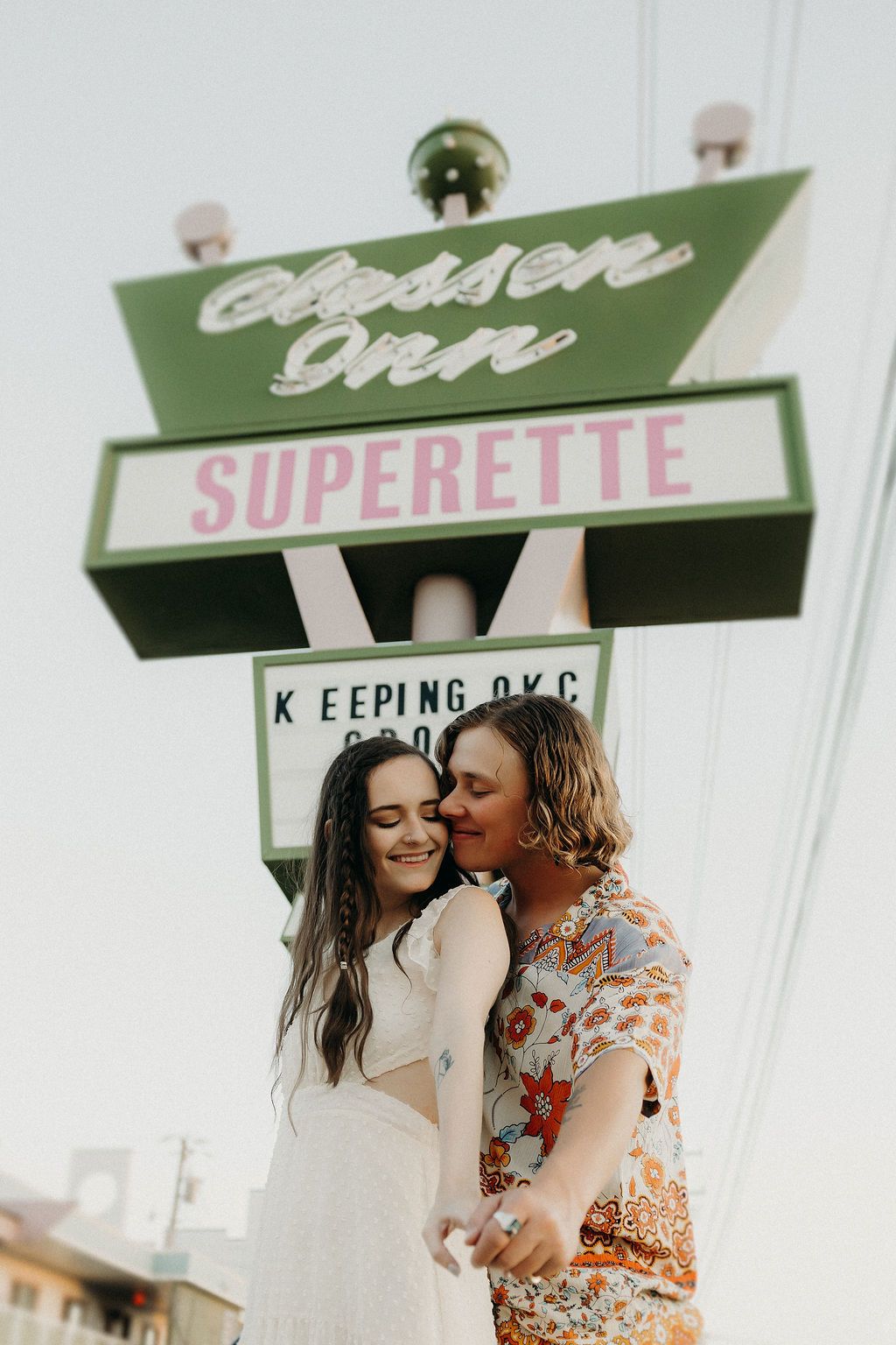 A couple shares a tender moment under a vintage Superette sign.