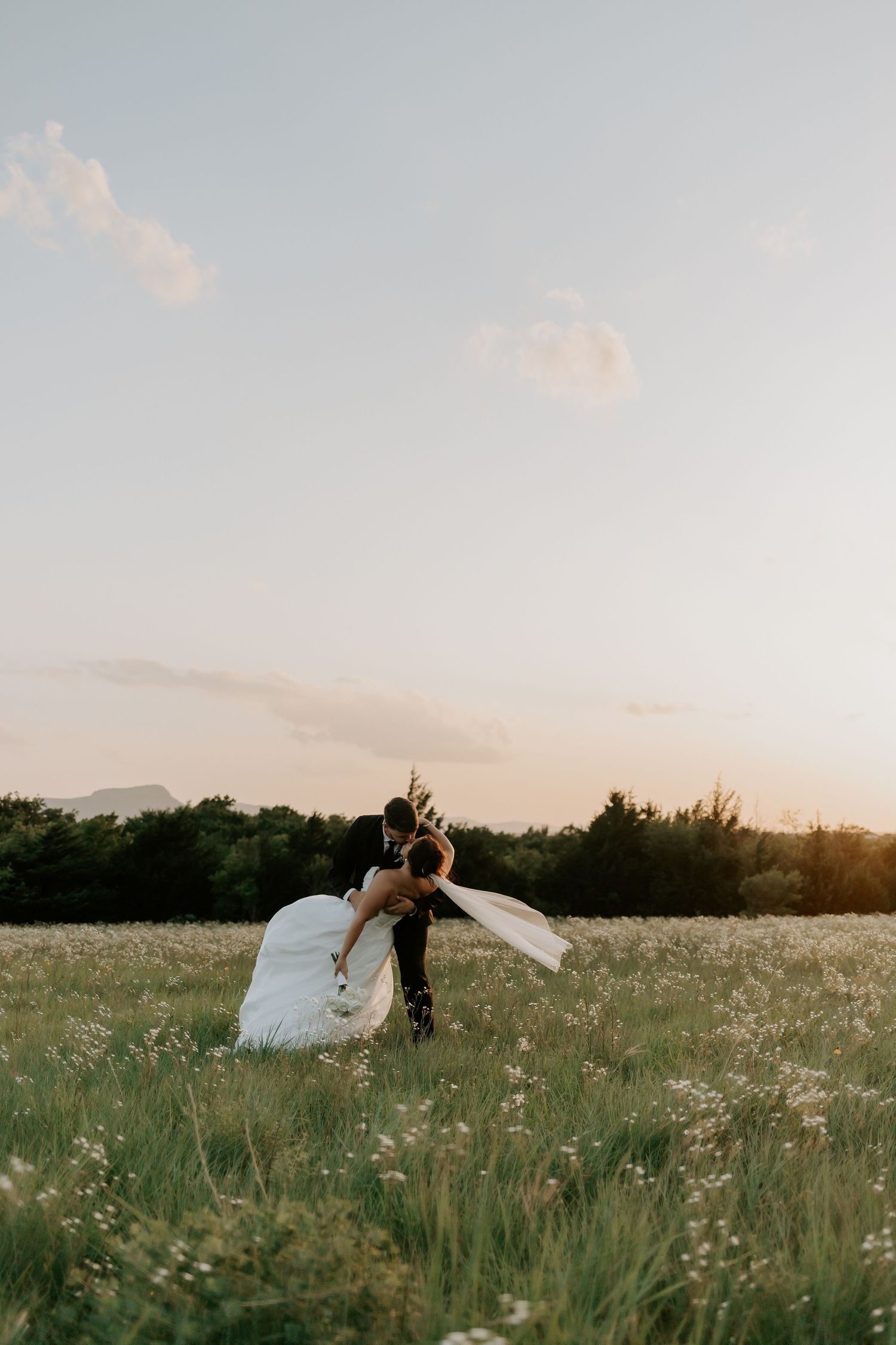 Dramatic sunset kiss in wildflower field with flowing veil.
