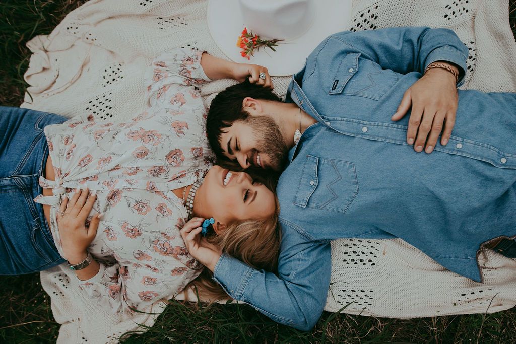 Couple lying on floral blanket during outdoor photo session.