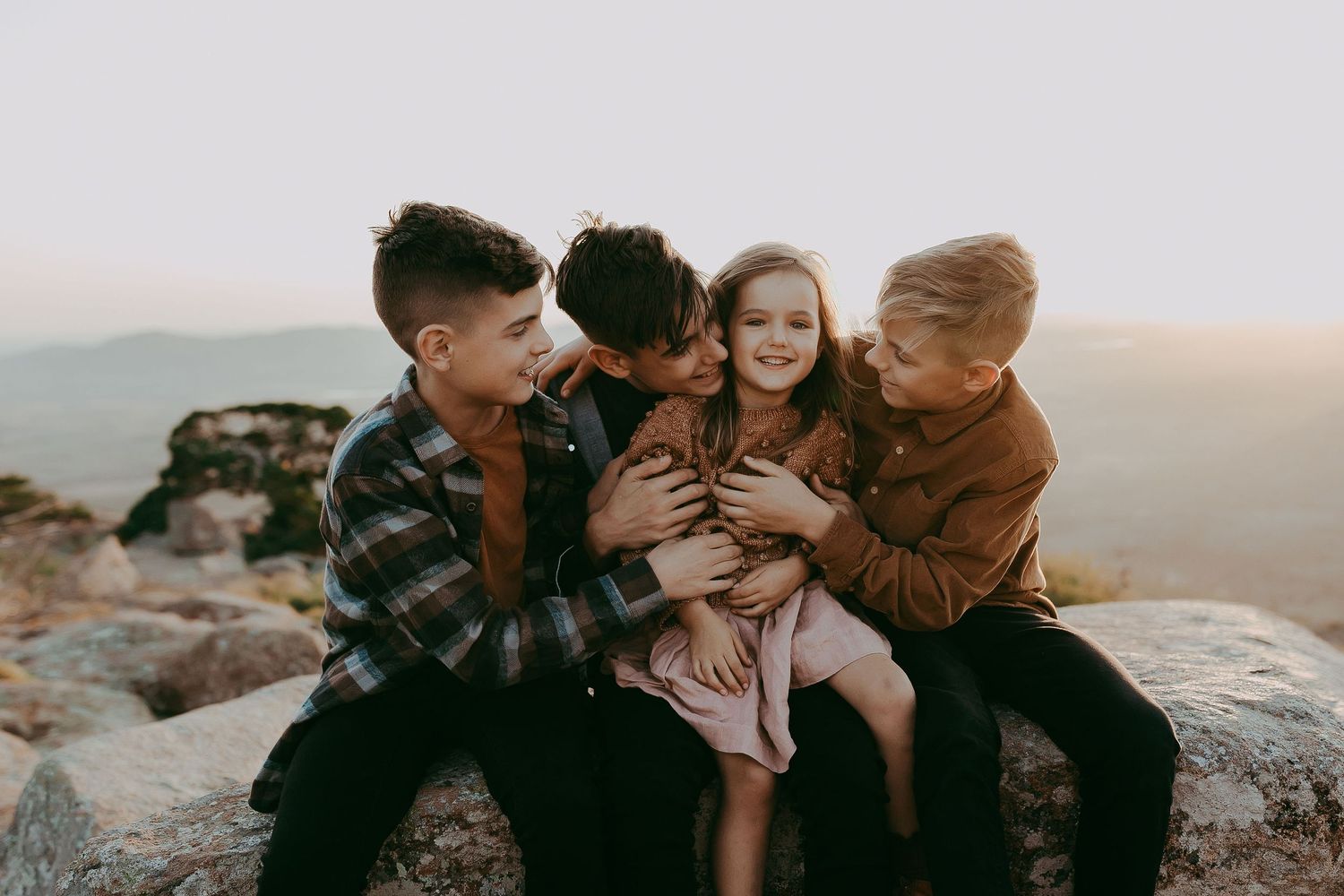 Family sitting together on rocky outcrop during sunset photoshoot.