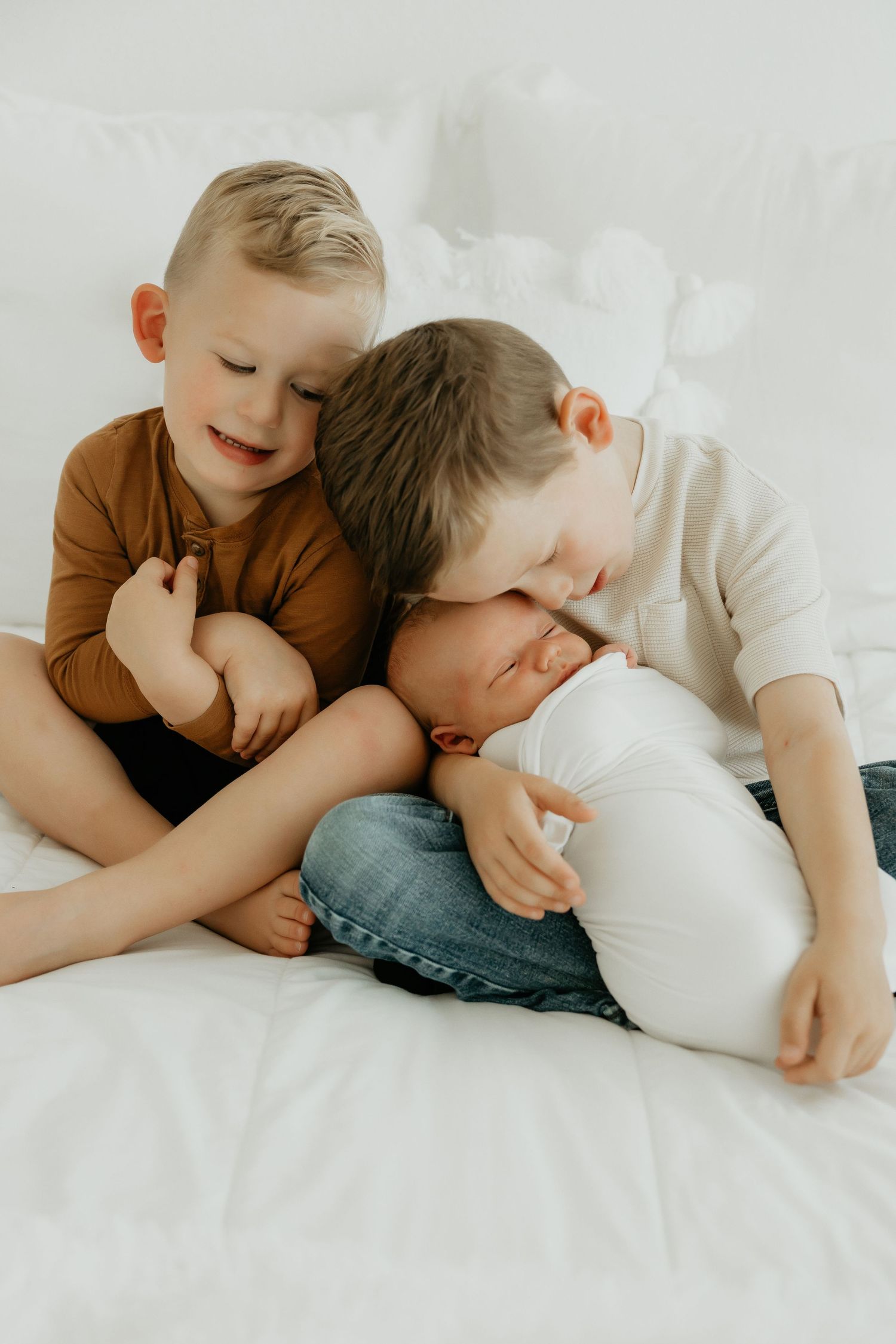 Two young children in brown shirts cuddle playfully on a white bed.