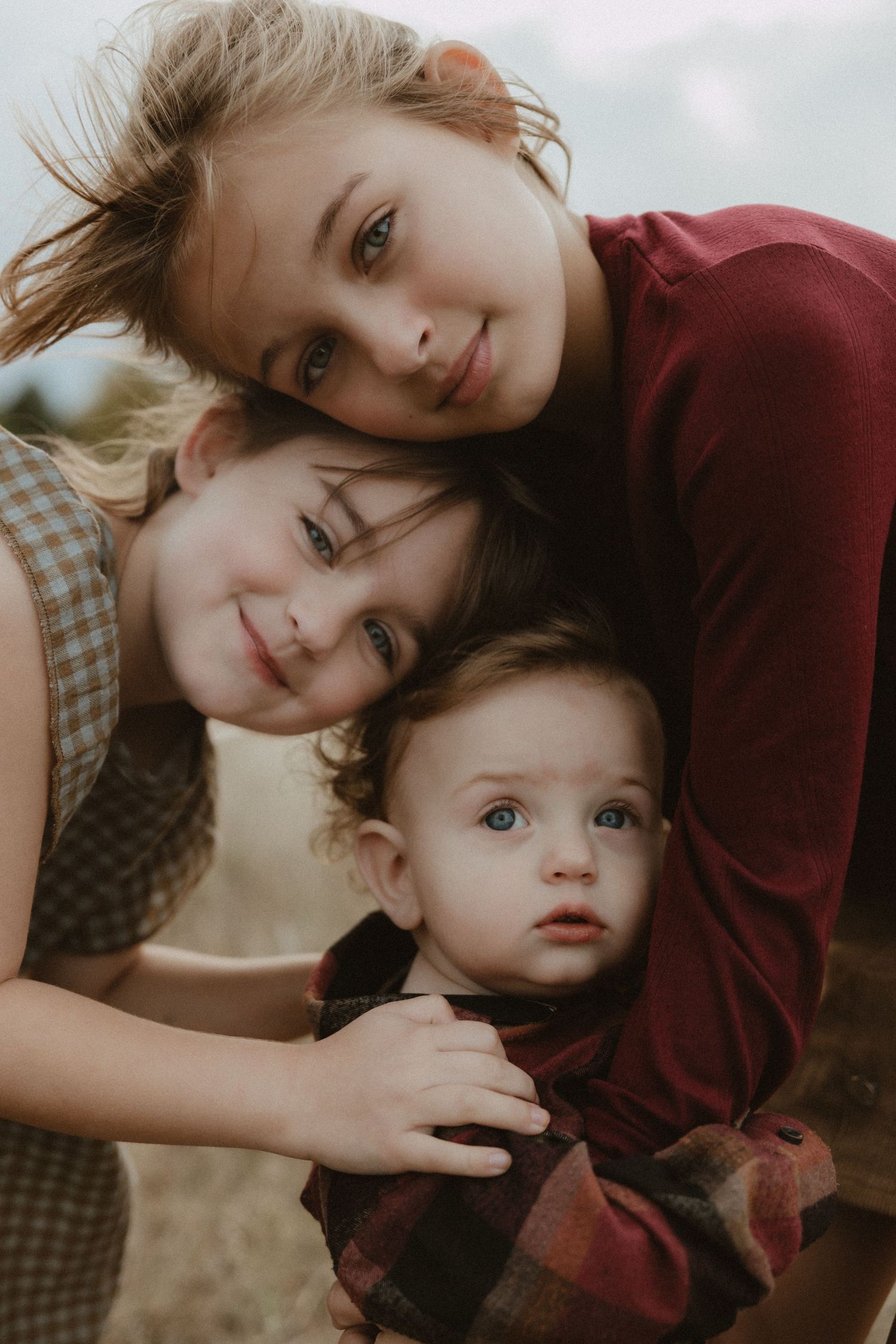 Intimate family portrait with burgundy and plaid clothing in soft lighting.