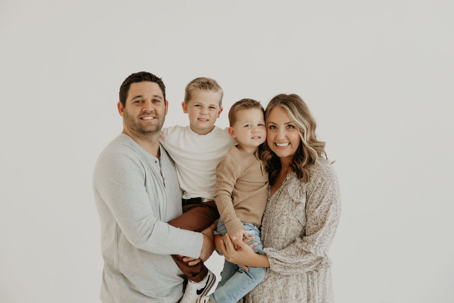 Studio family portrait with coordinating neutral outfits against light gray background.