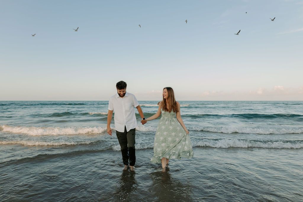 Couple wading into ocean waves during beach photoshoot.