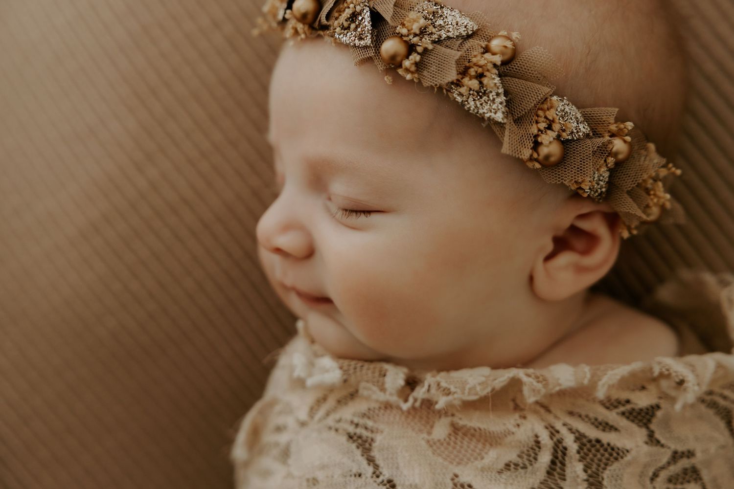 Sleeping newborn wearing ornate gold crown headpiece.