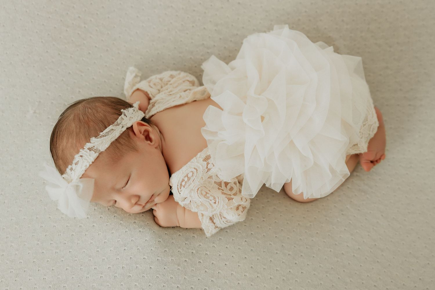 Baby wearing delicate white lace outfit while sleeping peacefully.