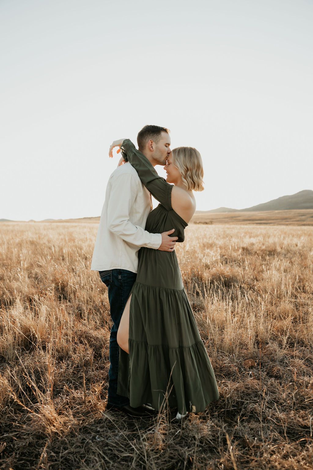 A couple embraces in a rustic field during golden hour.
