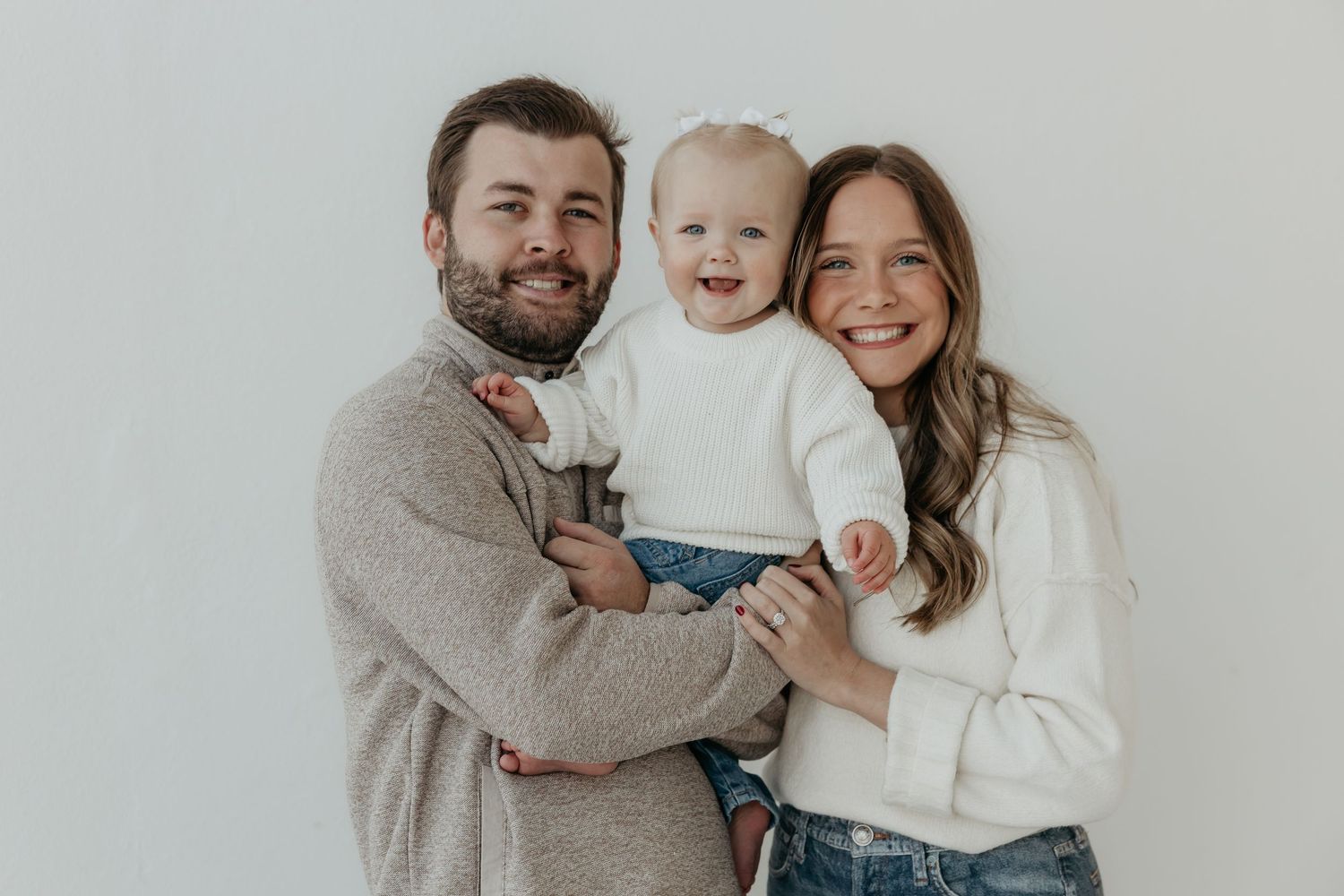Indoor family portrait session against white background in neutral colored clothing.