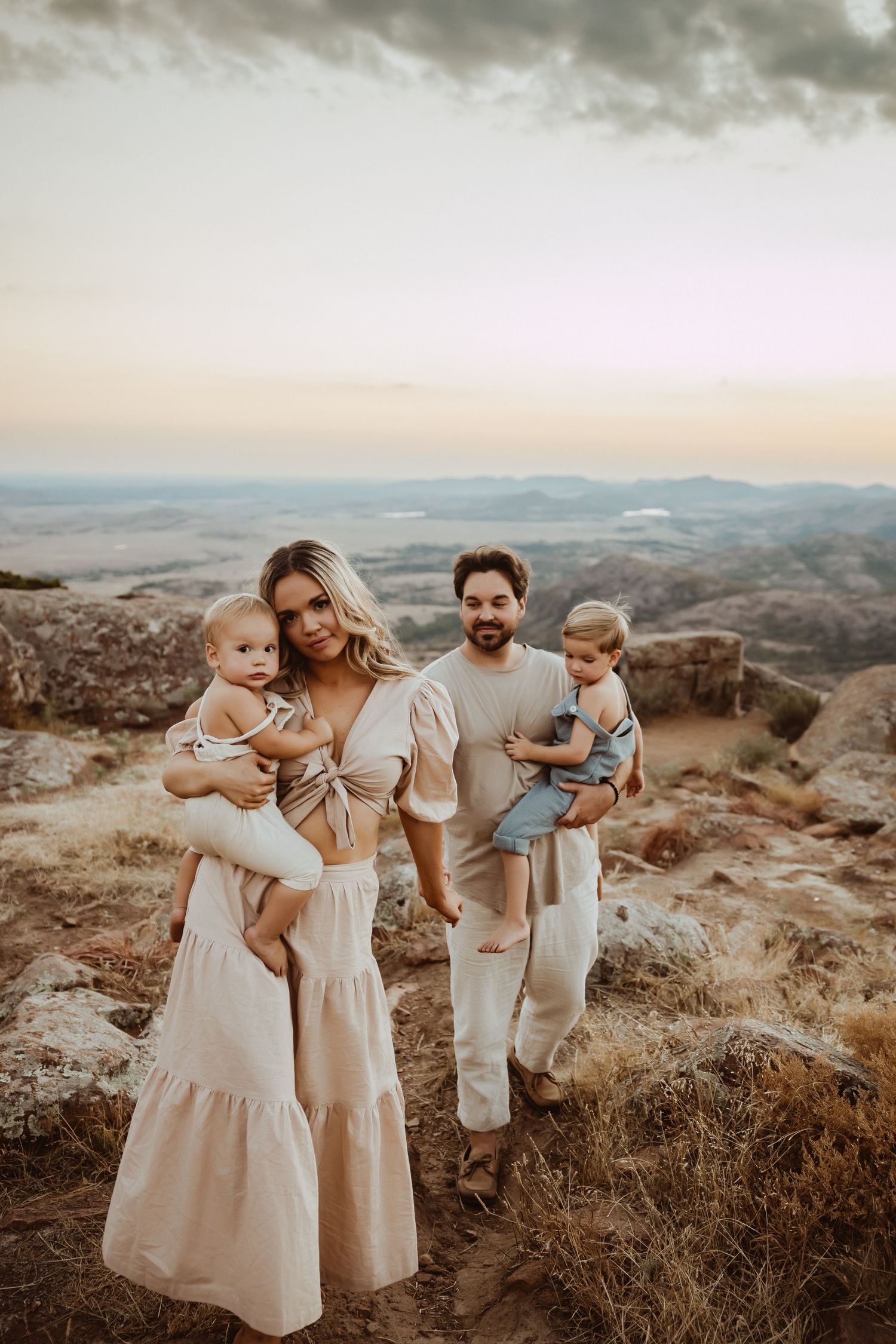 A family portrait session on a hilltop during sunset wearing coordinated neutral outfits.