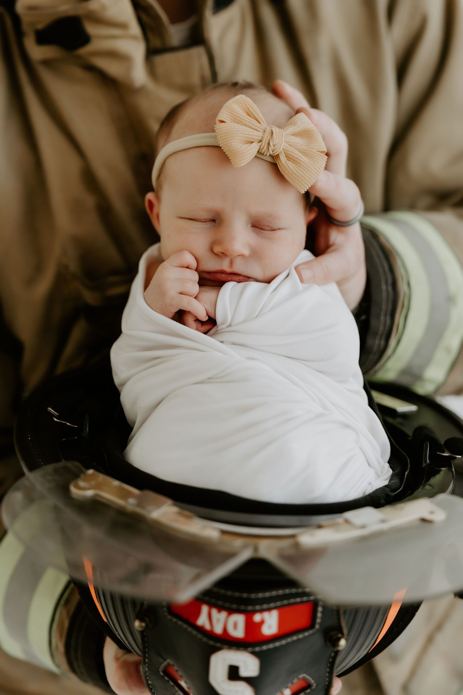 Sleeping newborn with bow headband nestled in firefighter gear.