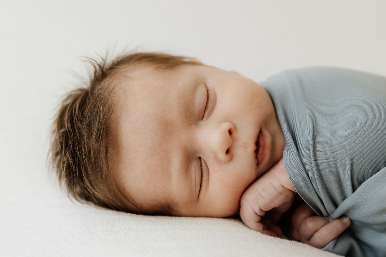 Sleeping baby in soft gray clothing against light background.