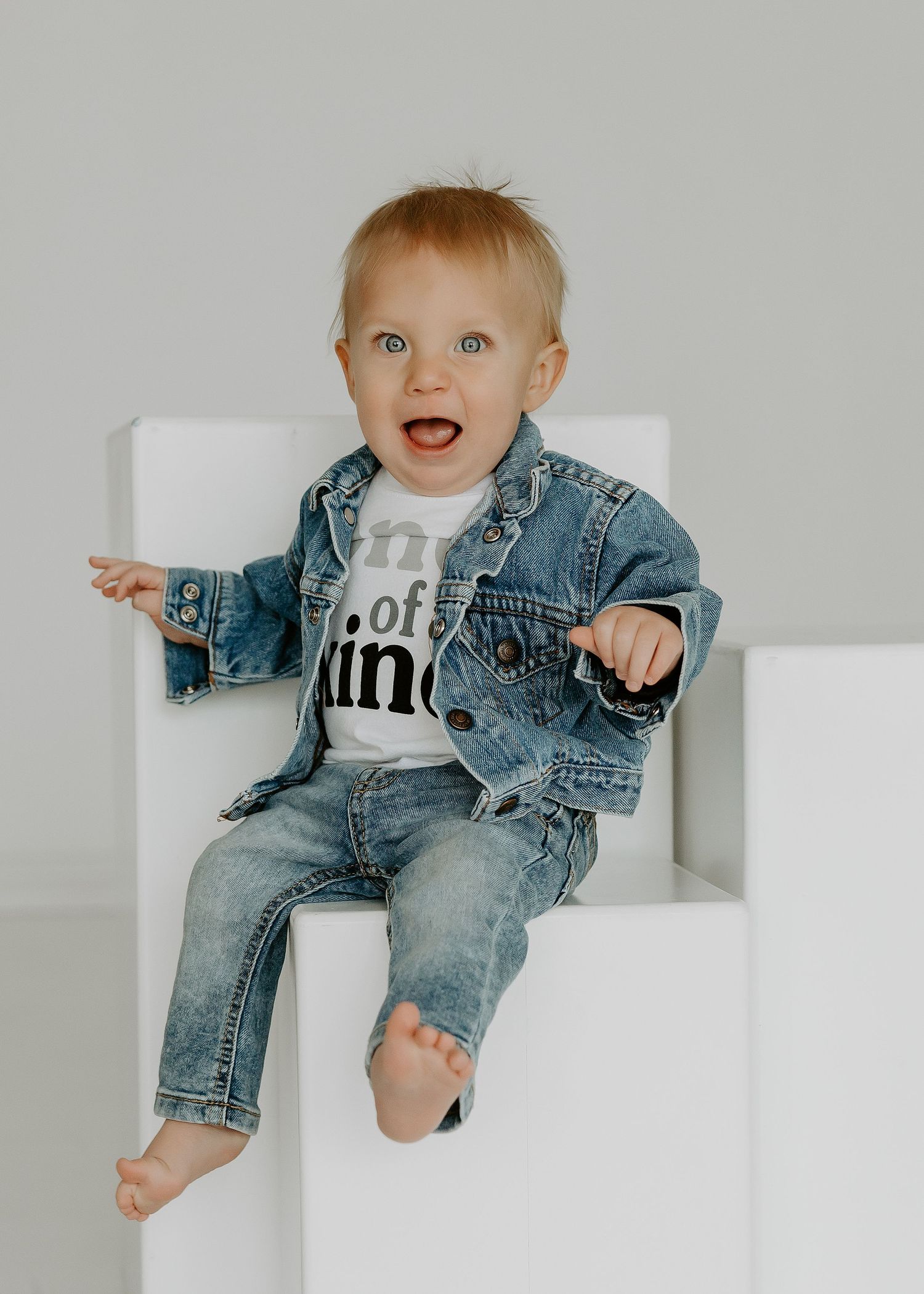 Baby in denim jacket sitting on white ledge.