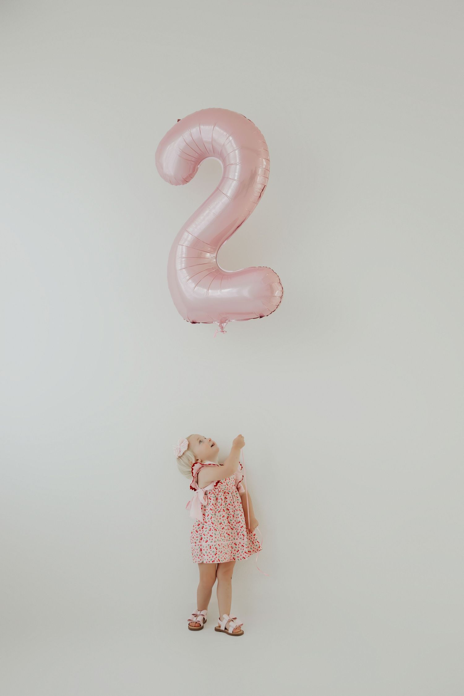 Pink number 2 balloon floats above stuffed toy against white wall.
