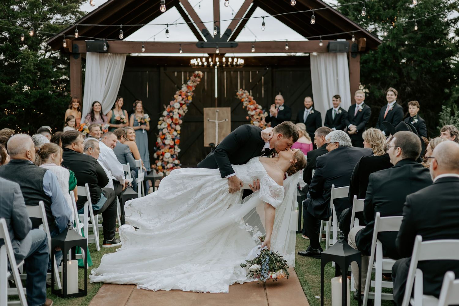 Outdoor wedding ceremony setup with wooden beams and floral arch decorations.