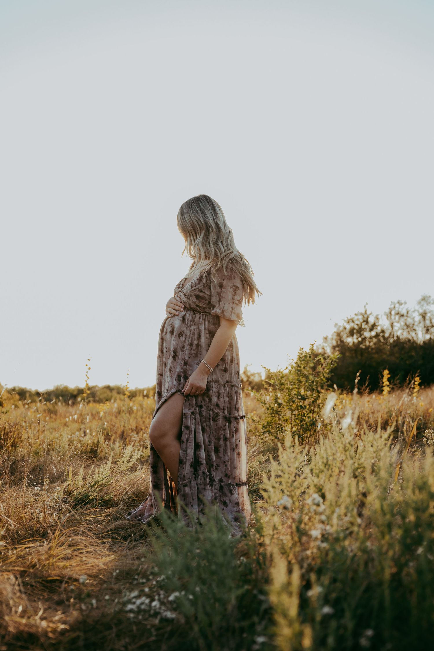 Silhouette of person in floral dress walking through golden field at sunset.