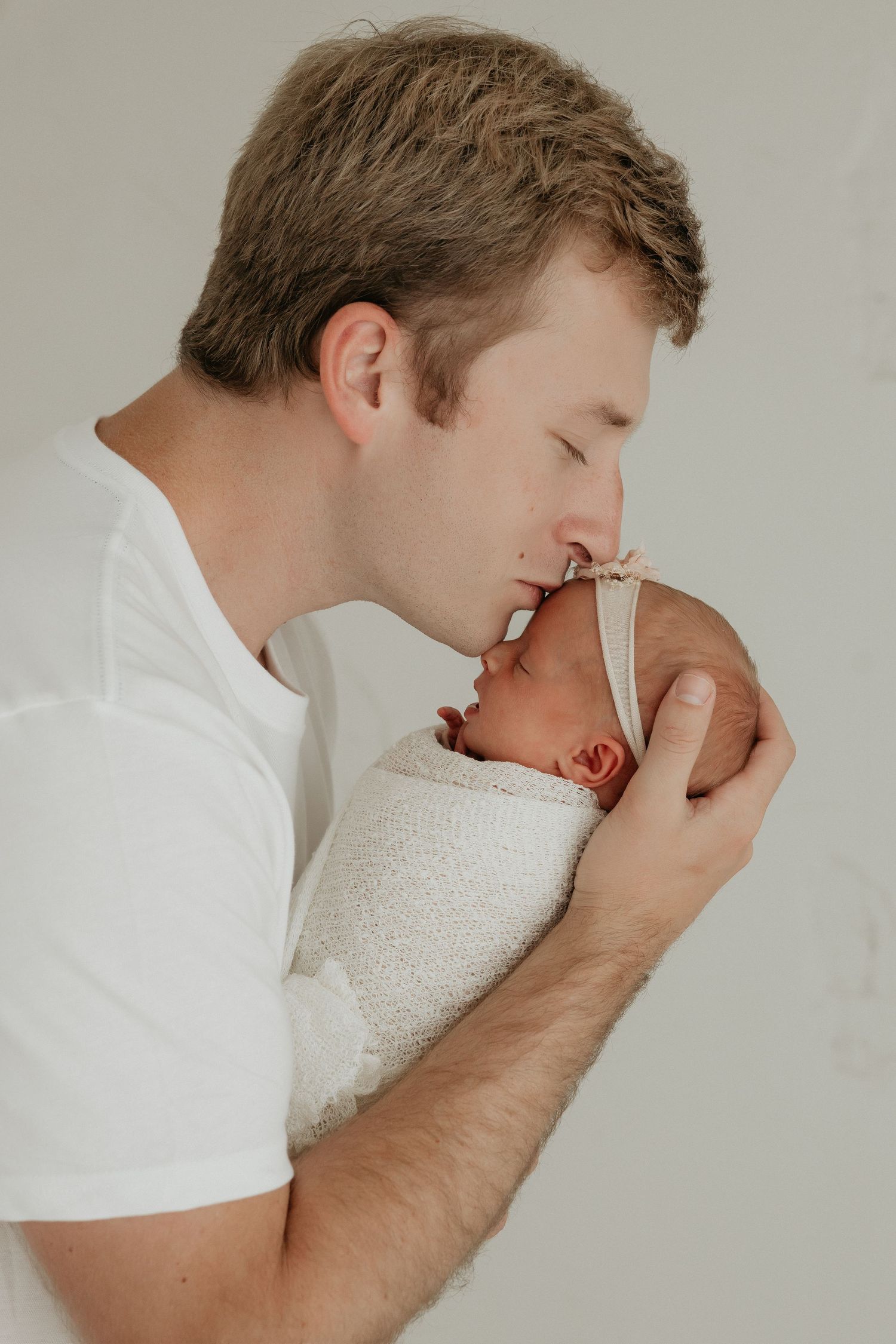 Tender moment between parent and baby in white setting.