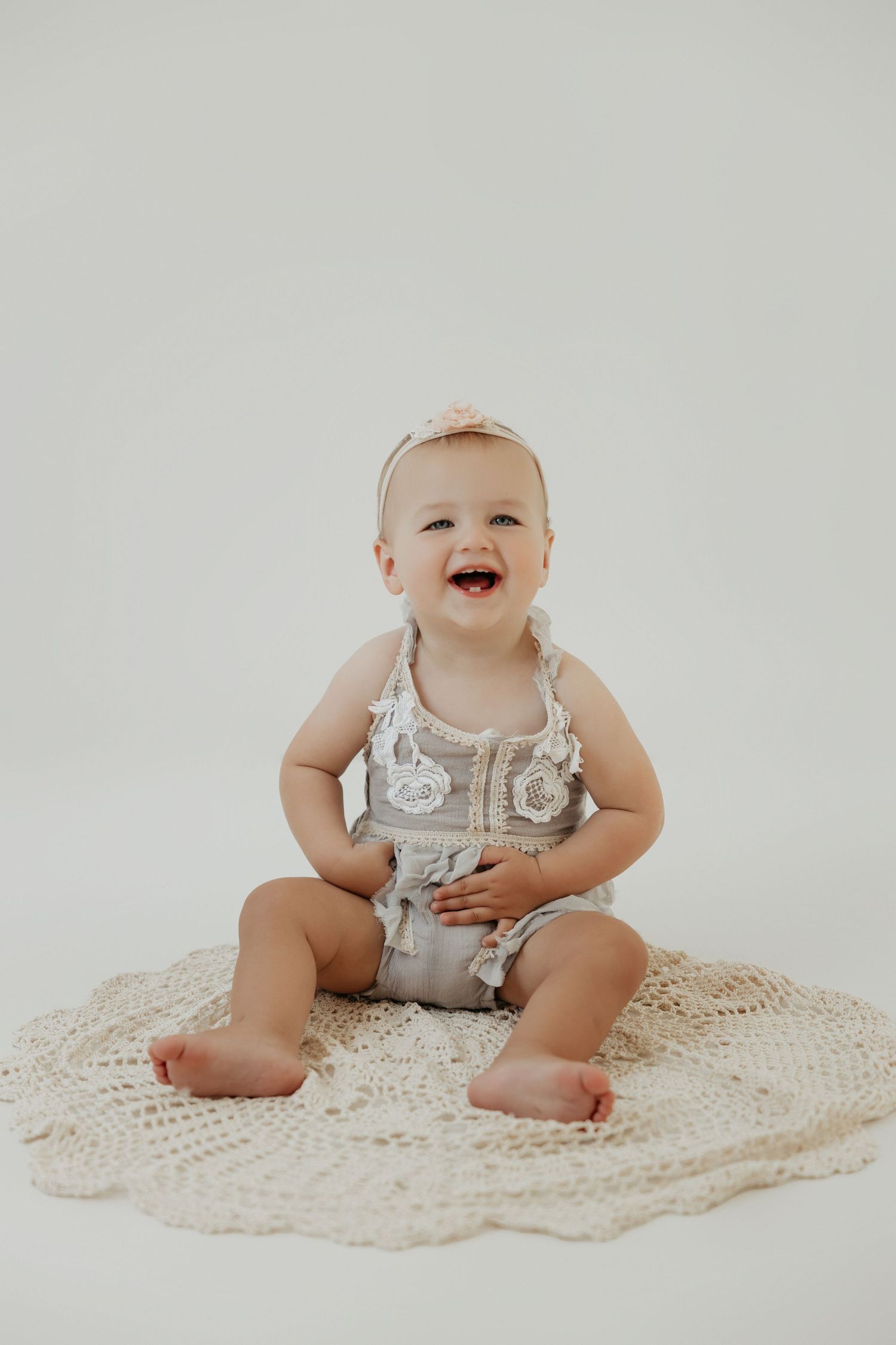 Baby in silver outfit sits smiling on cream knit blanket.