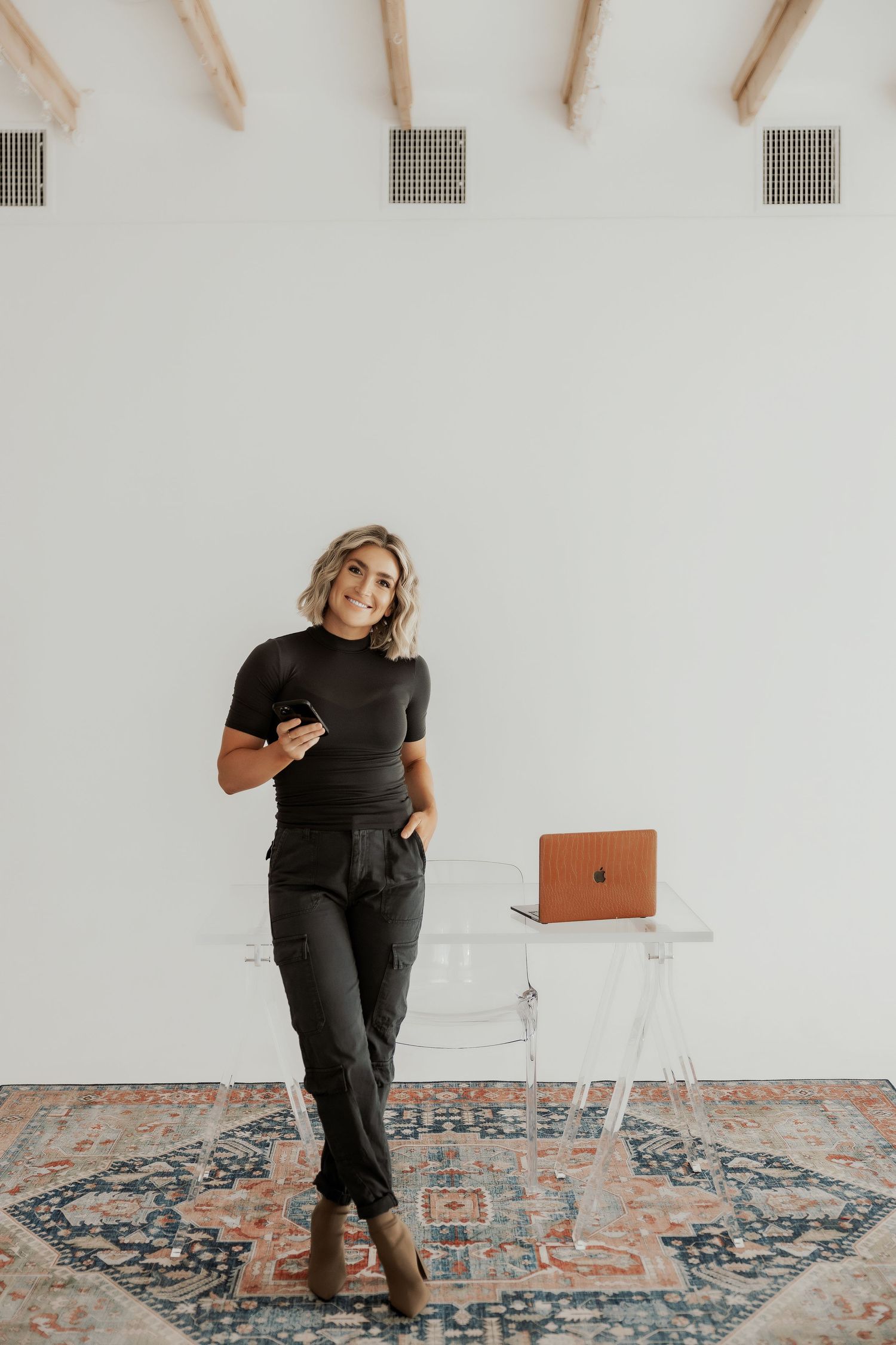 Playful poses on patterned rug wearing all black outfit in minimalist space.