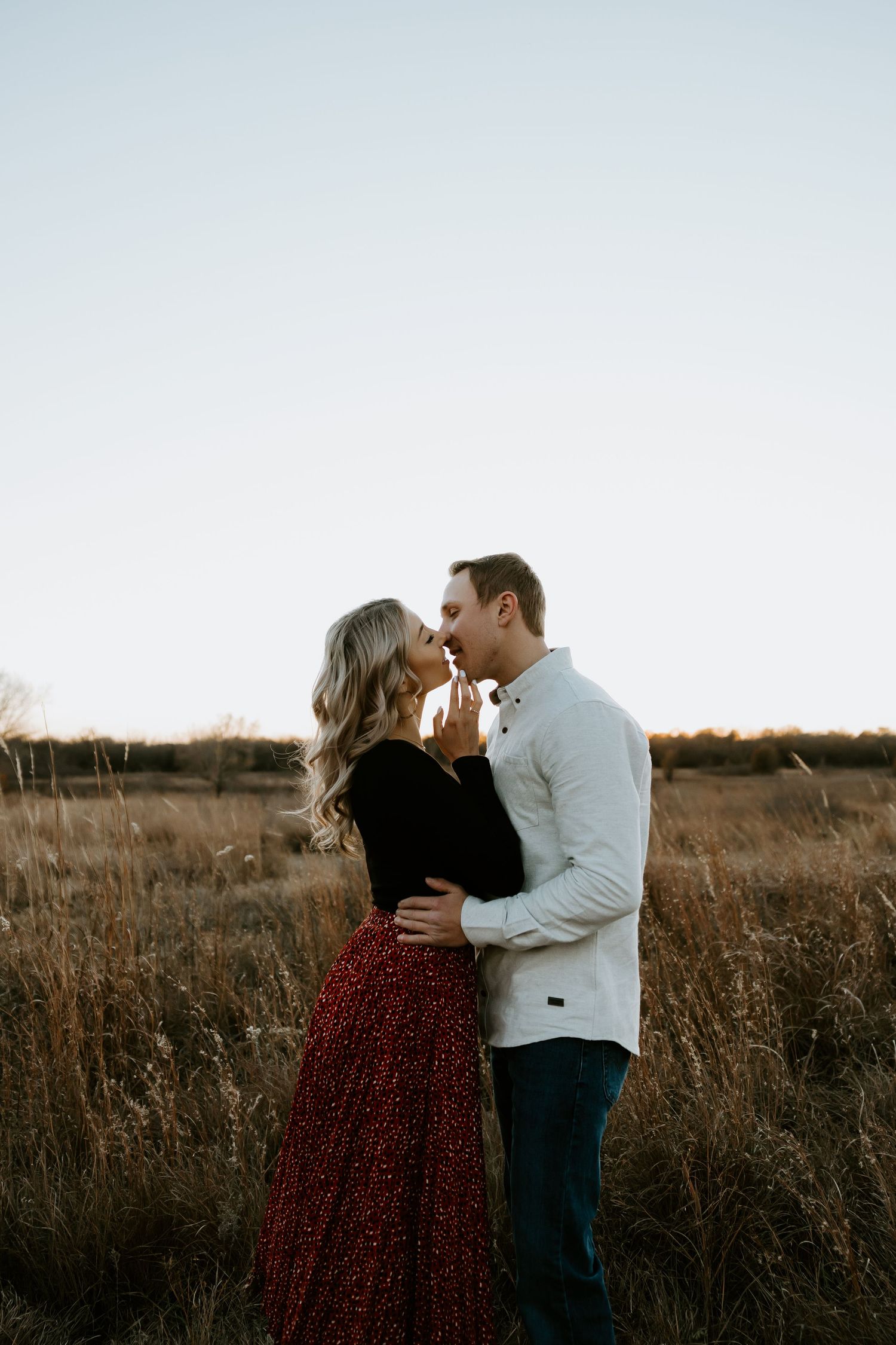 A romantic couple embraces in a golden field during sunset.