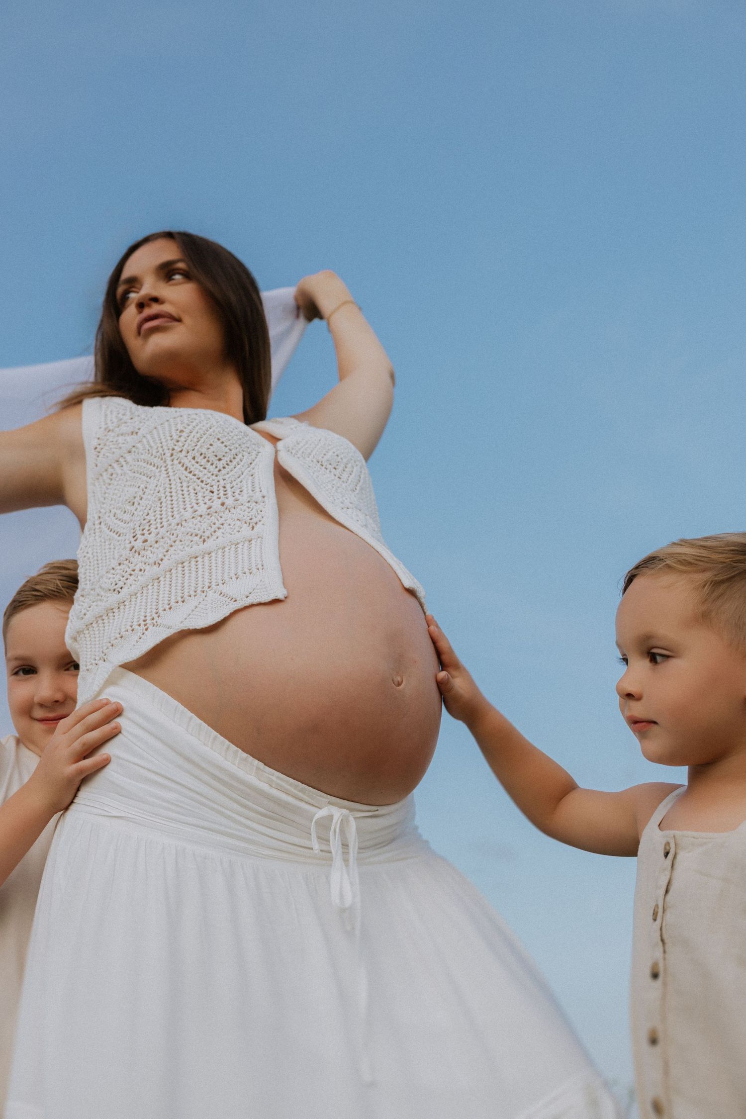 Close-up details of white lace maternity dress against blue sky.