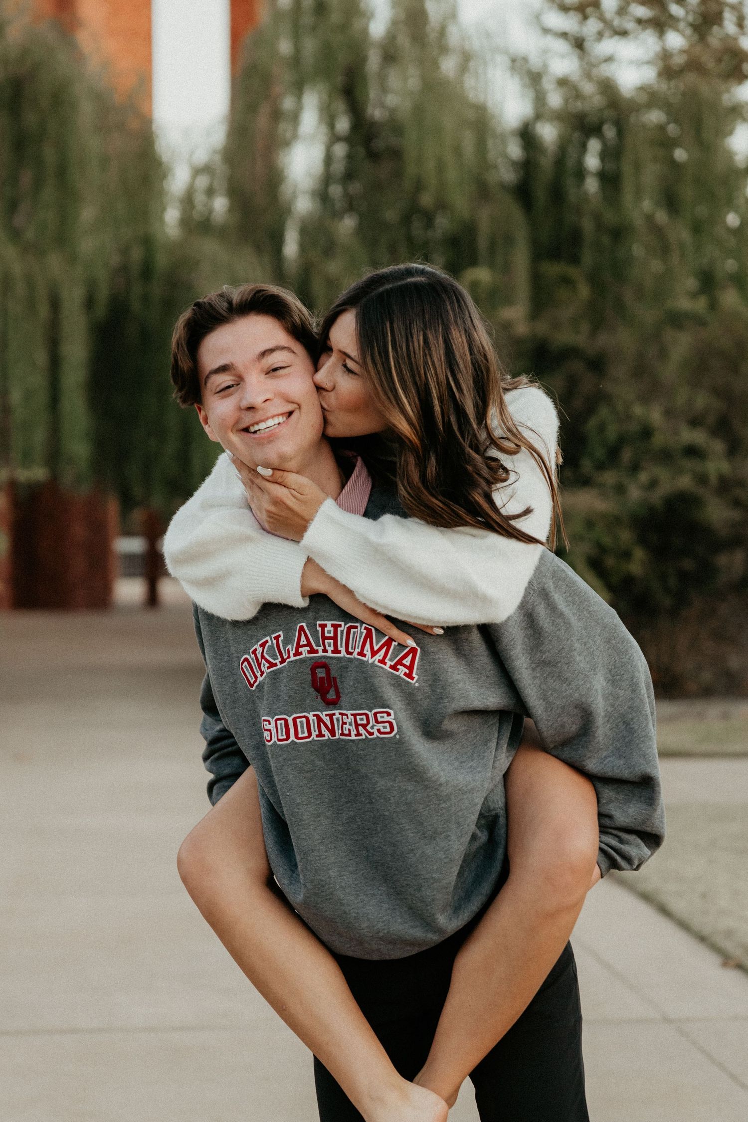 Couple wearing Oklahoma Sooners sweatshirt sharing affectionate moments outdoors.