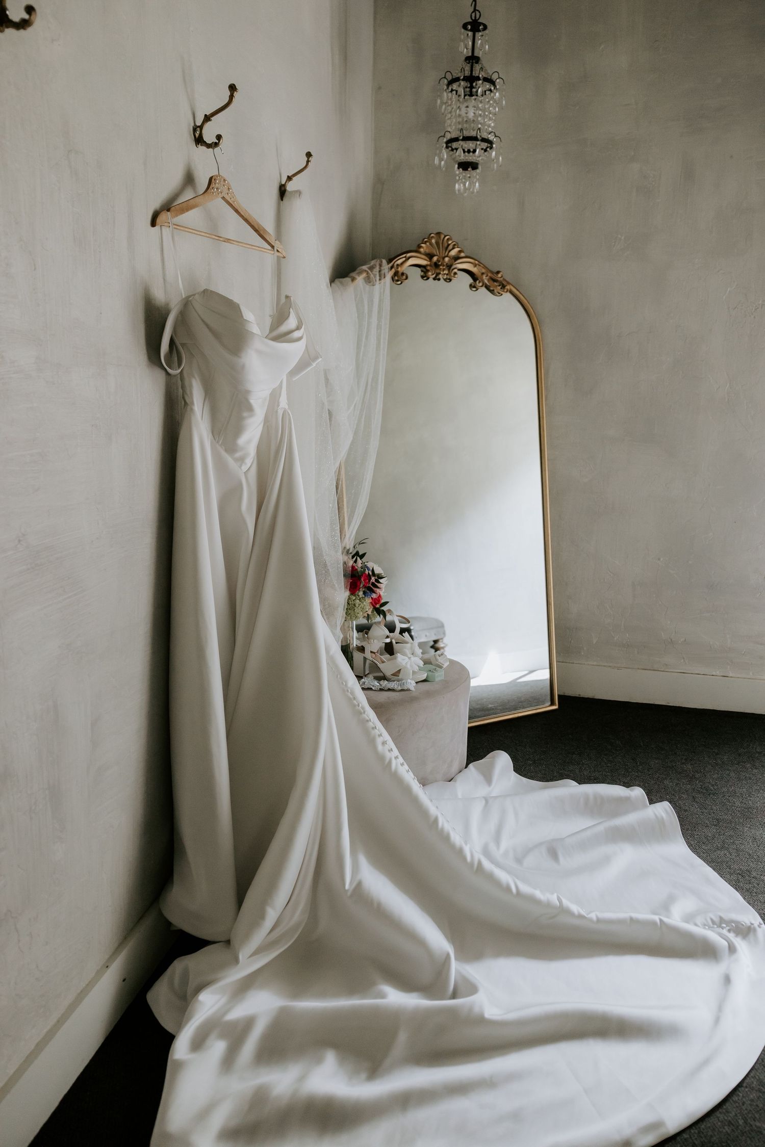 Elegant white wedding dress displayed against grey walls with flowing train and floral details.
