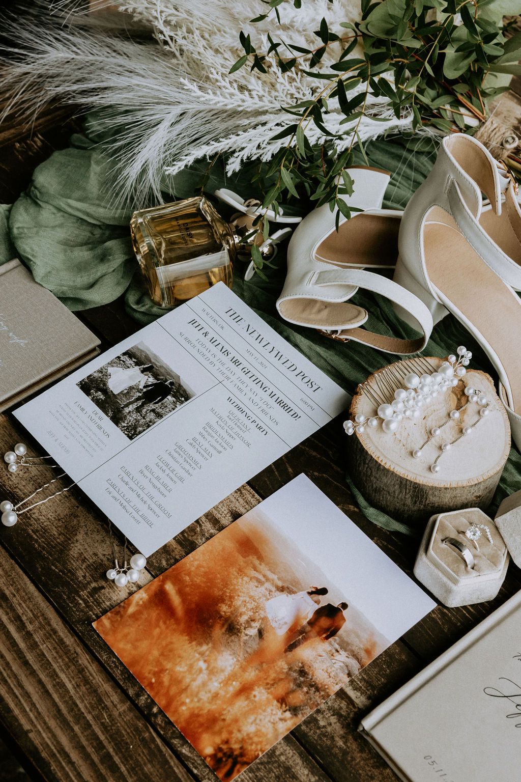 Wedding details flatlay with invitation, shoes, and floral elements on rustic wooden surface.