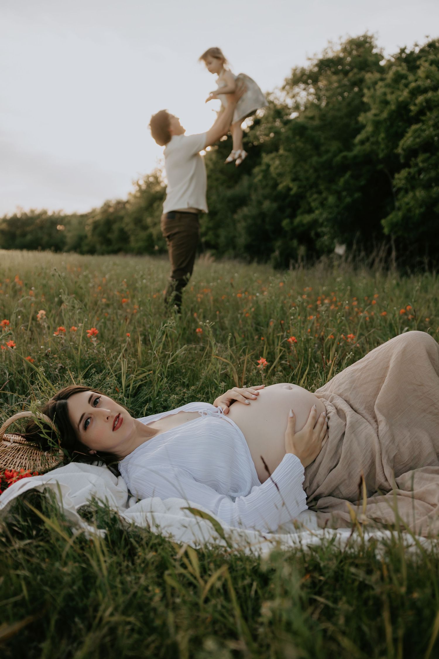 Person lying in grass field surrounded by red wildflowers during golden hour.
