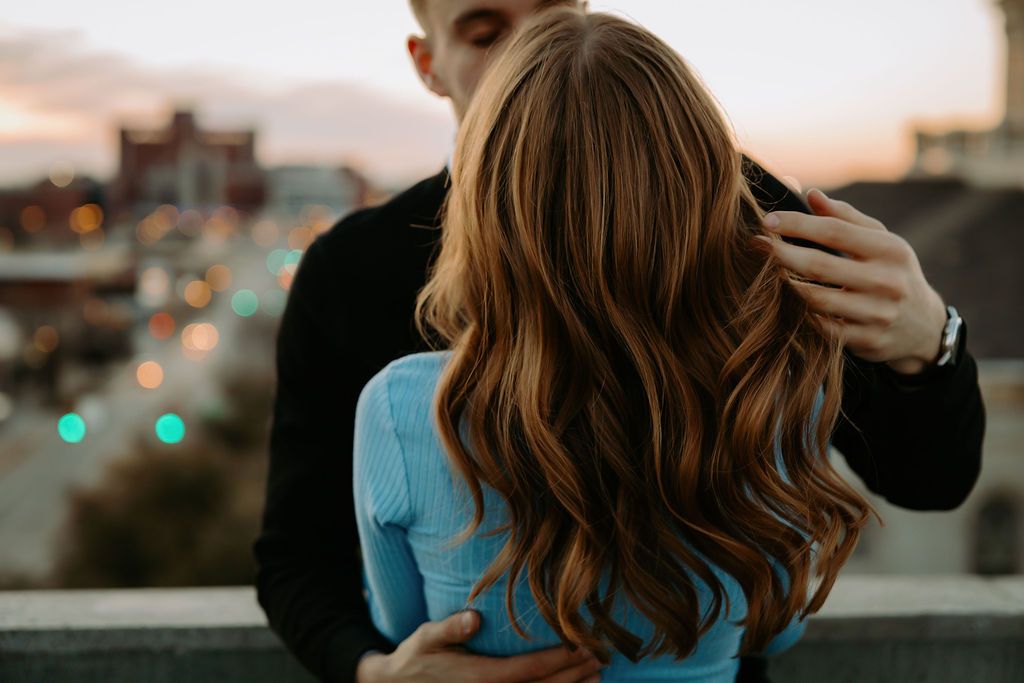 Couple sharing intimate moment at sunset with city lights in background.