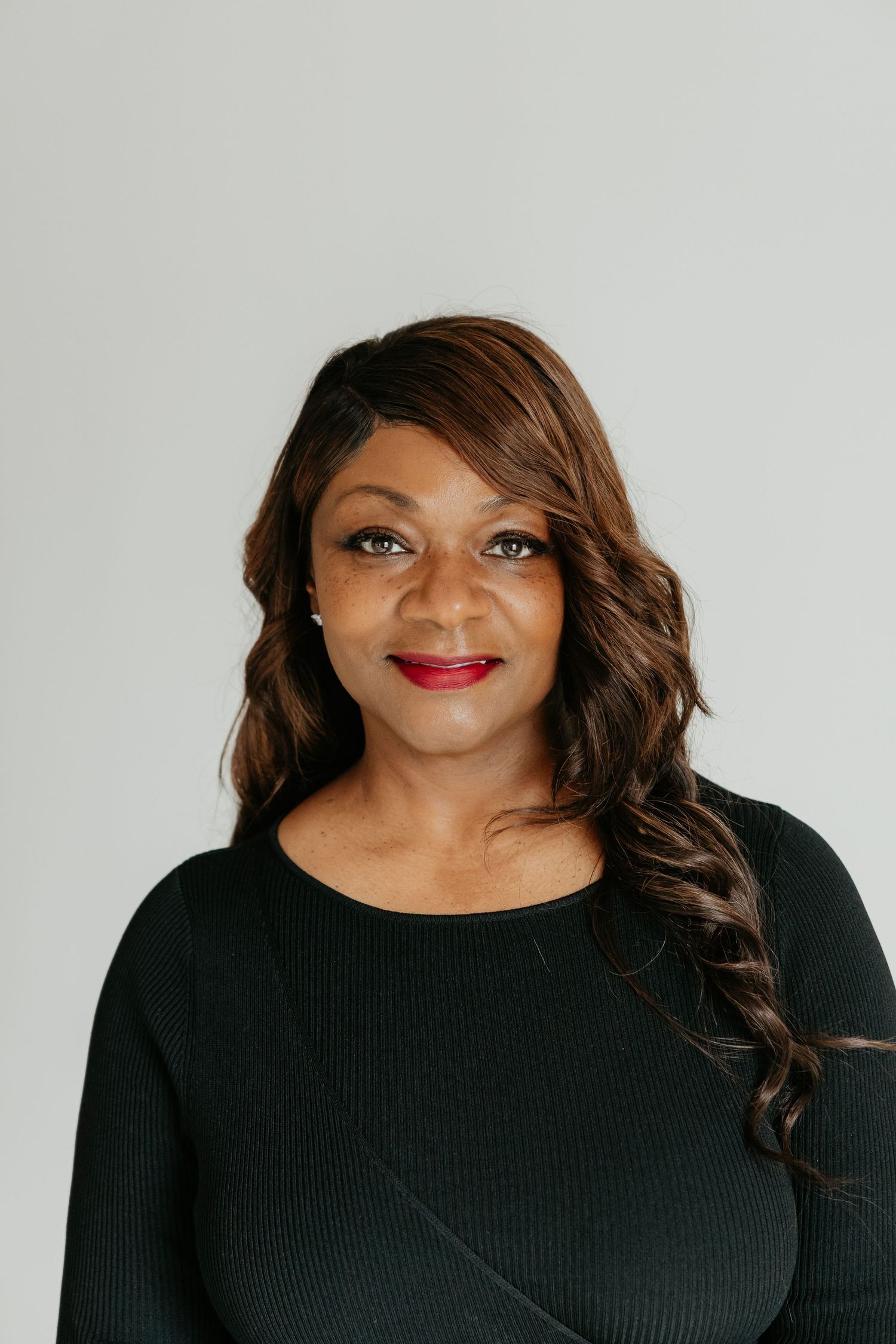 Studio portrait of person in black top with styled hair against white backdrop.