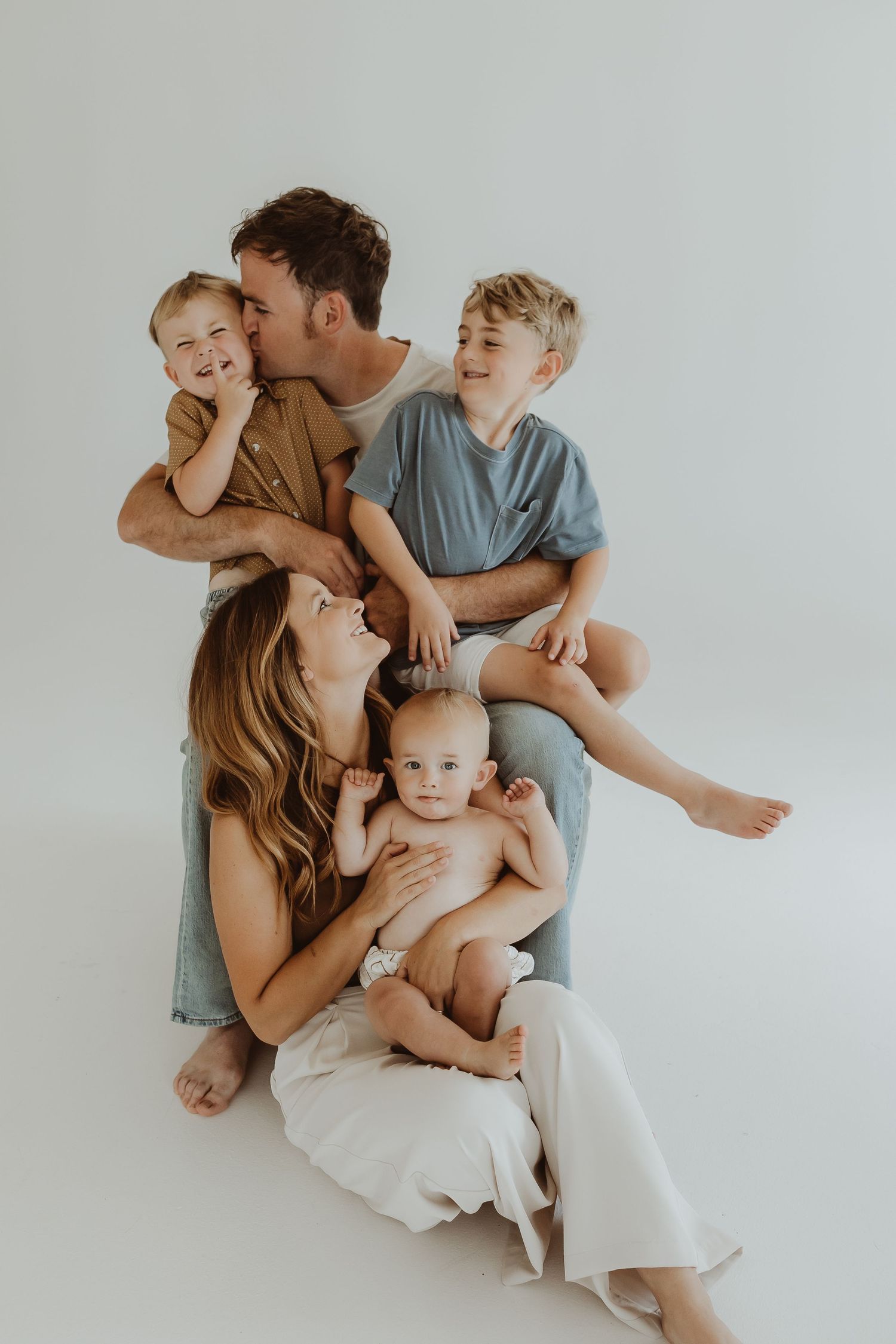 Family cuddling together on white background in casual attire.
