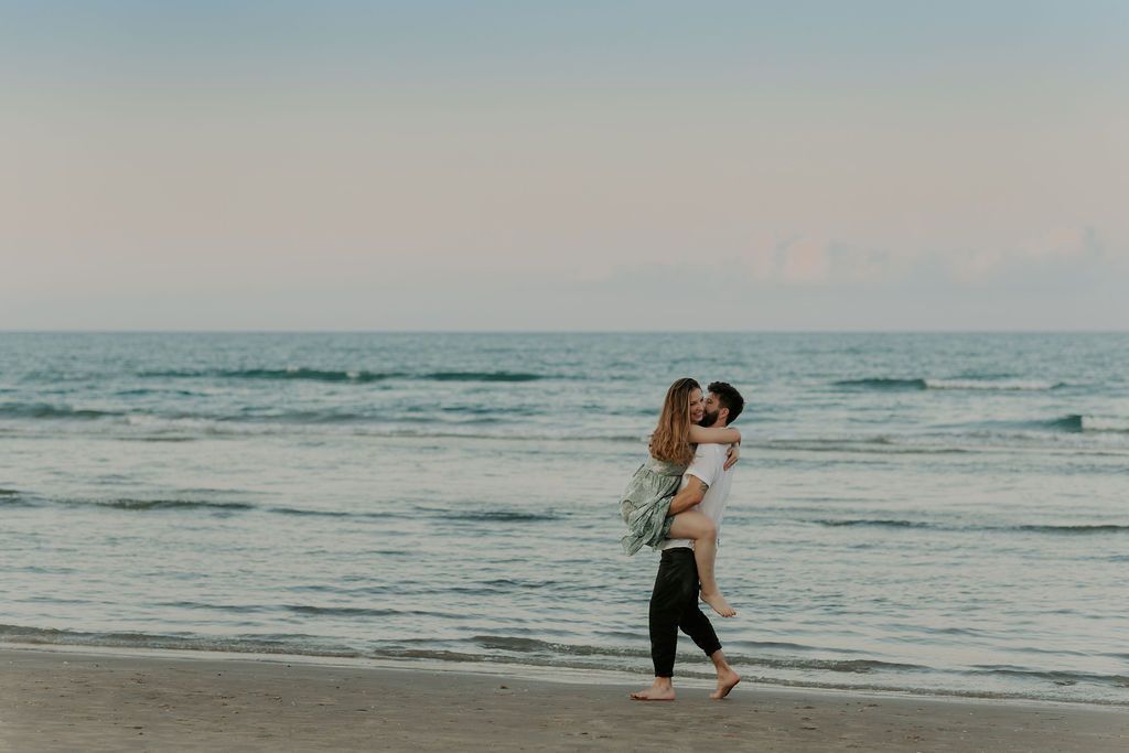 Couple walking and playing along ocean shoreline at sunset.