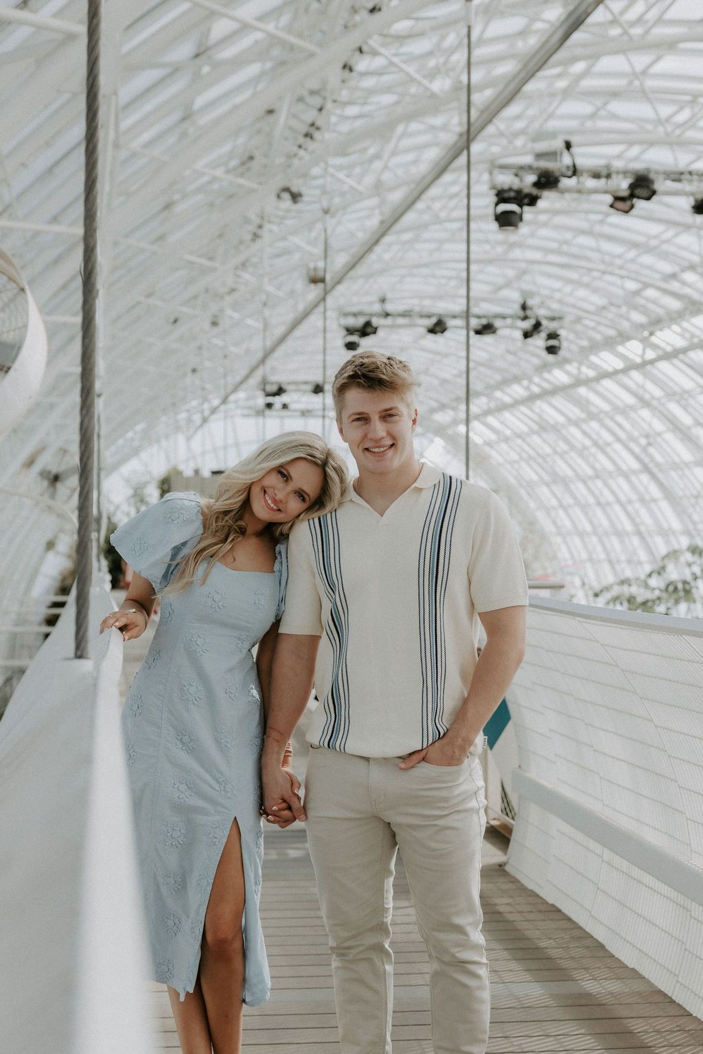 Couple sharing intimate moments in light-filled greenhouse hallway.