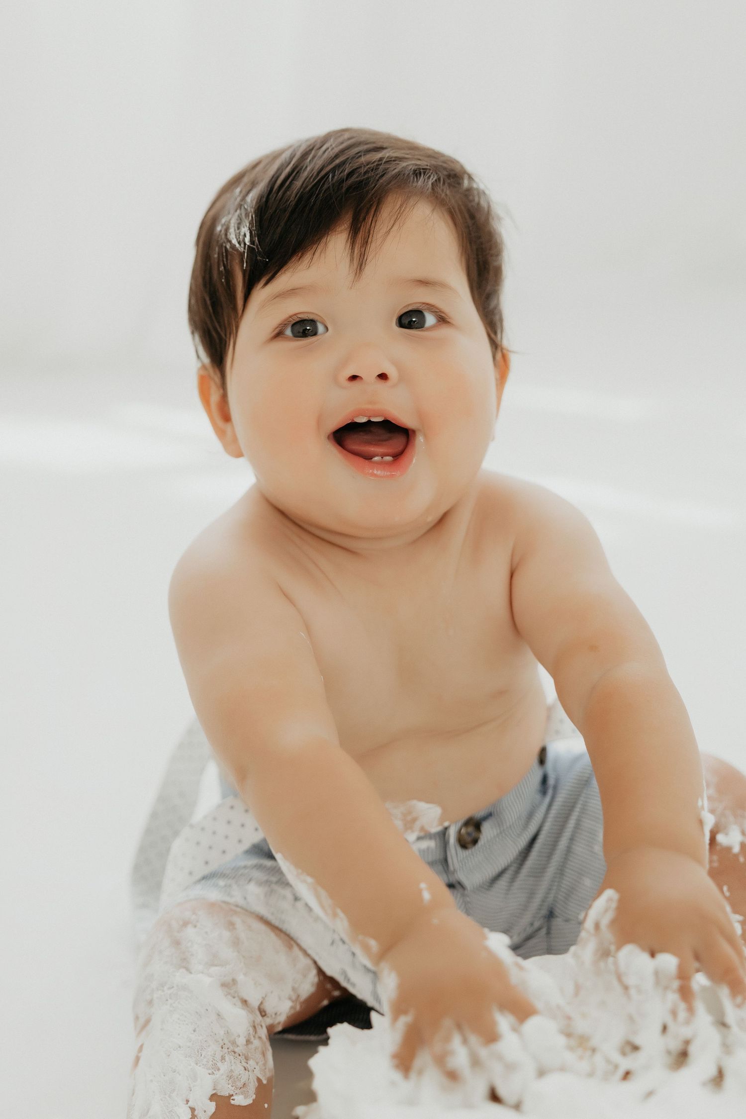 Baby explores and plays with white frosting during cake smash photo session.
