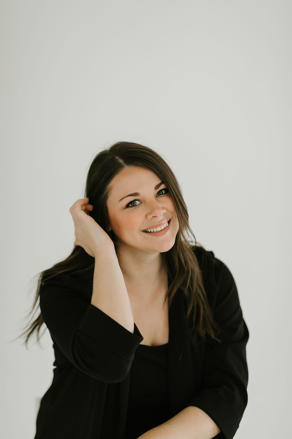 Studio portrait of someone in black attire touching their hair against white background.