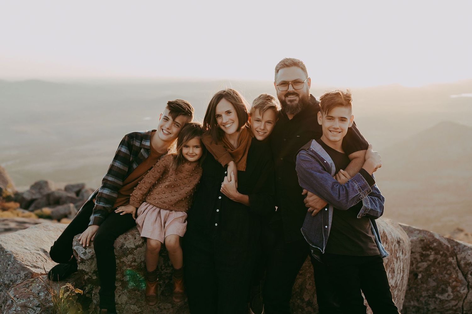 Group embracing on a hilltop overlooking a scenic mountain landscape.