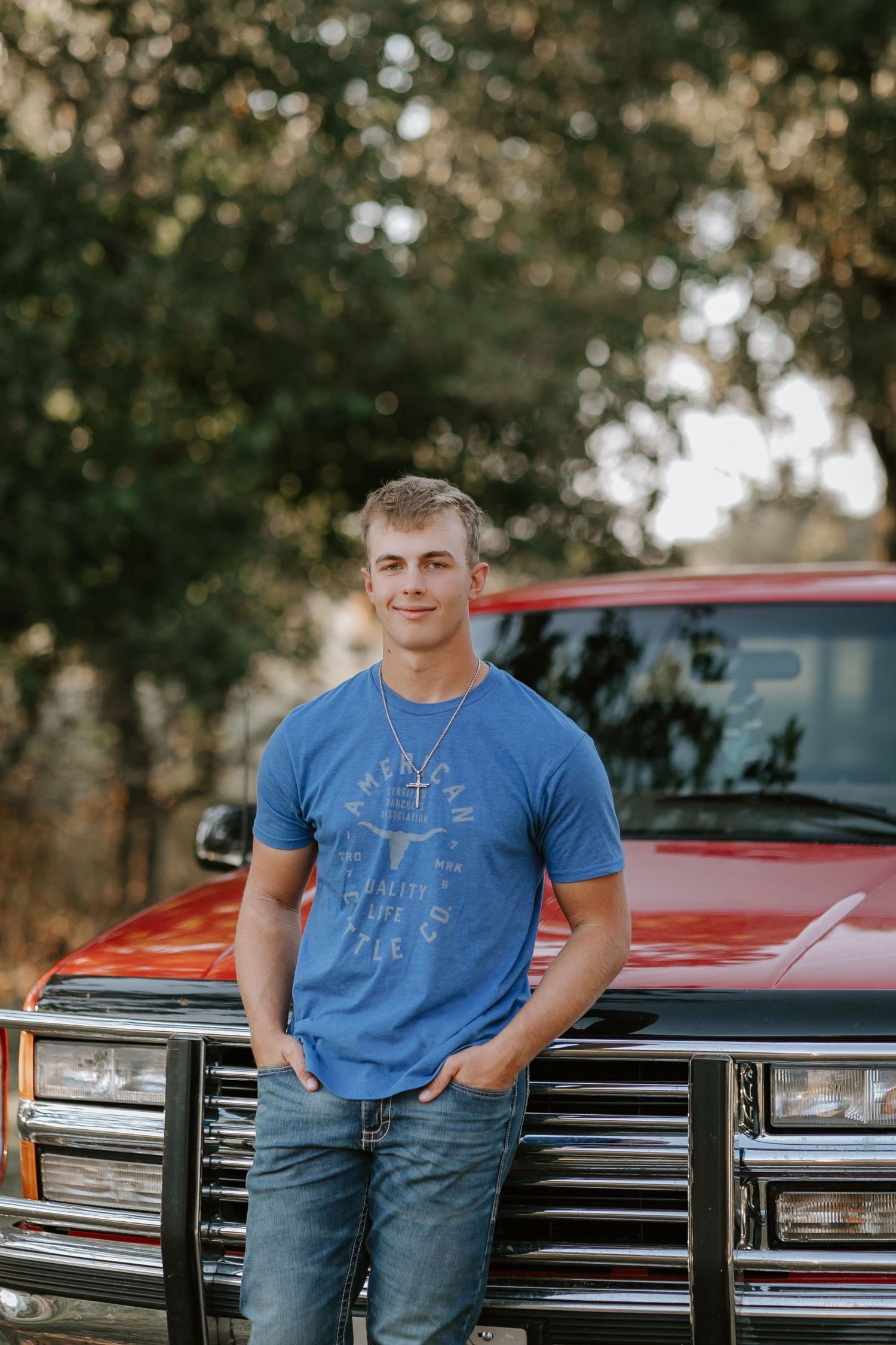 Person in blue t-shirt poses against vintage red truck during outdoor photoshoot.