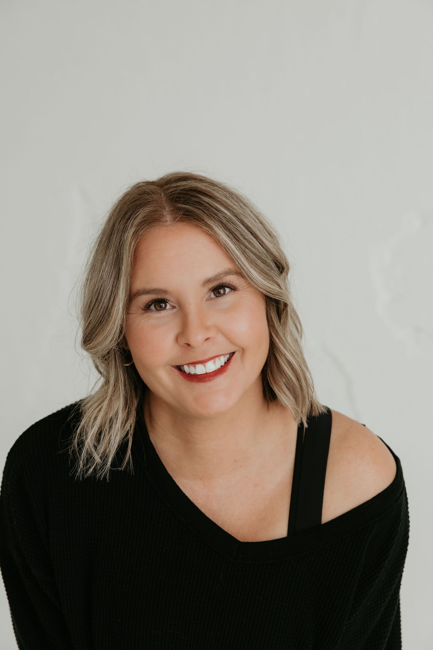 Studio portrait with blonde hair and black top against minimal white background.