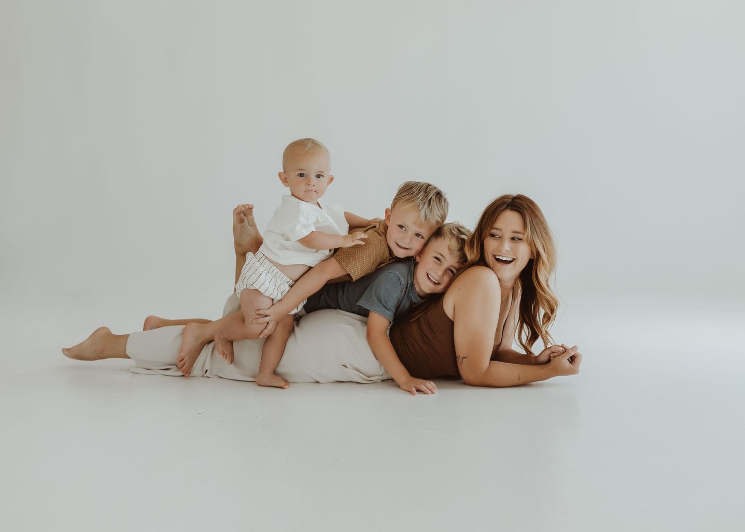 Family lying together on white floor in coordinated neutral outfits.