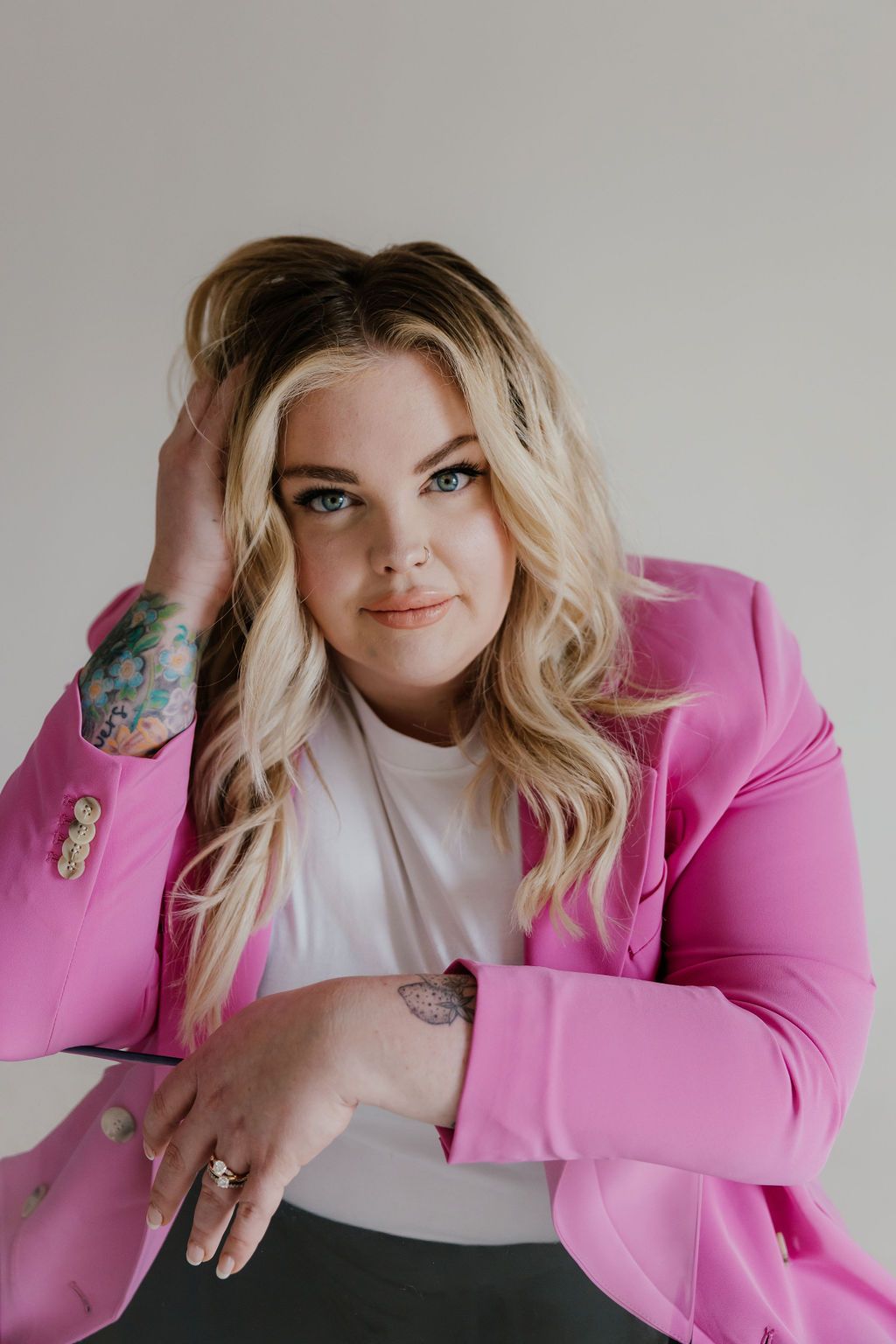 Portrait of someone wearing a bright pink blazer and white top with visible arm tattoos.