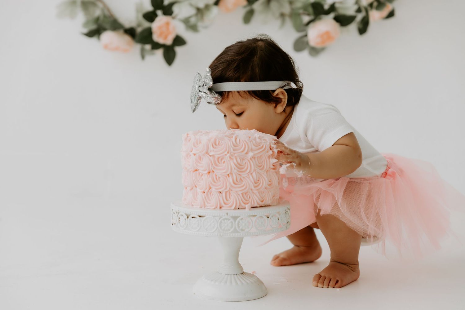 Baby in pink tulle dress crawling near floral decorations.