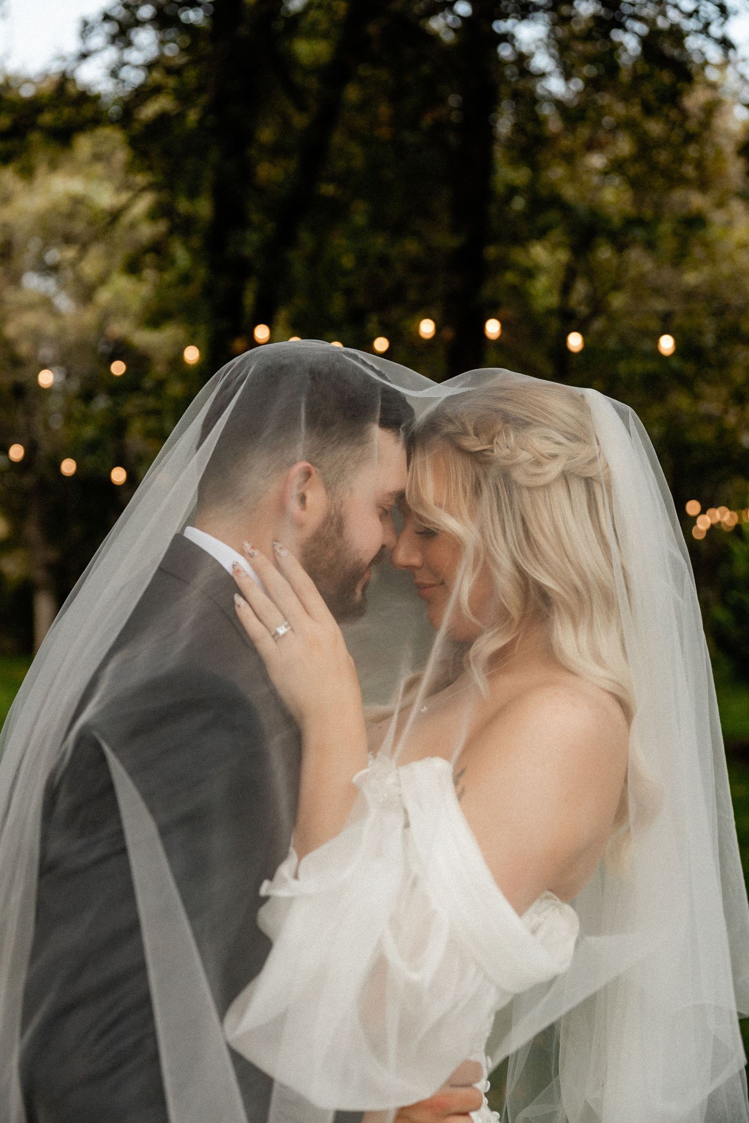 Romantic outdoor wedding portraits with string lights and flowing veil creating dreamy atmosphere.
