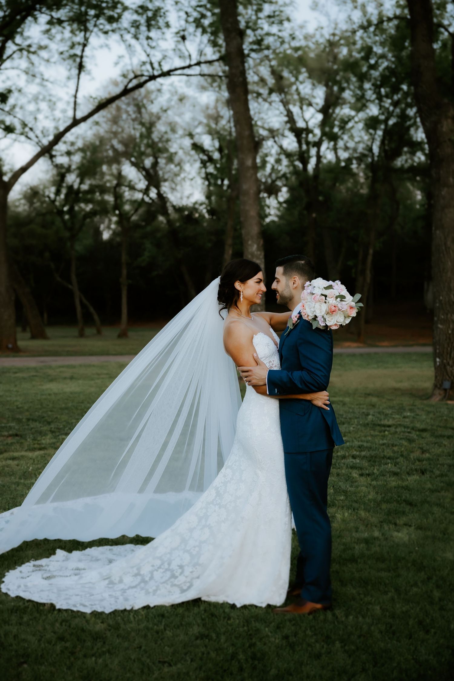Wedding couple in elegant attire sharing intimate moment in outdoor garden setting.