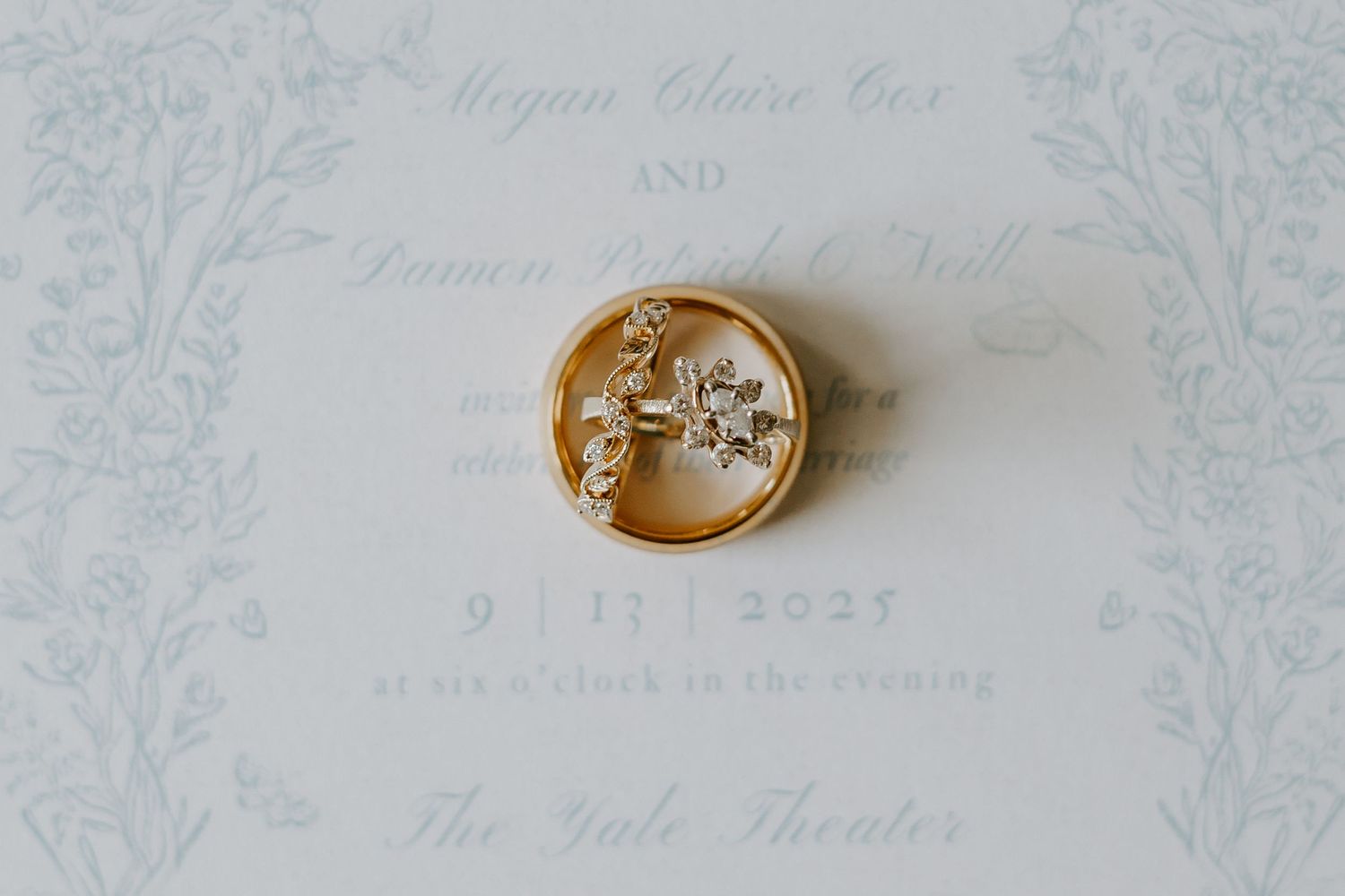 Delicate gold wedding rings on white invitation paper.