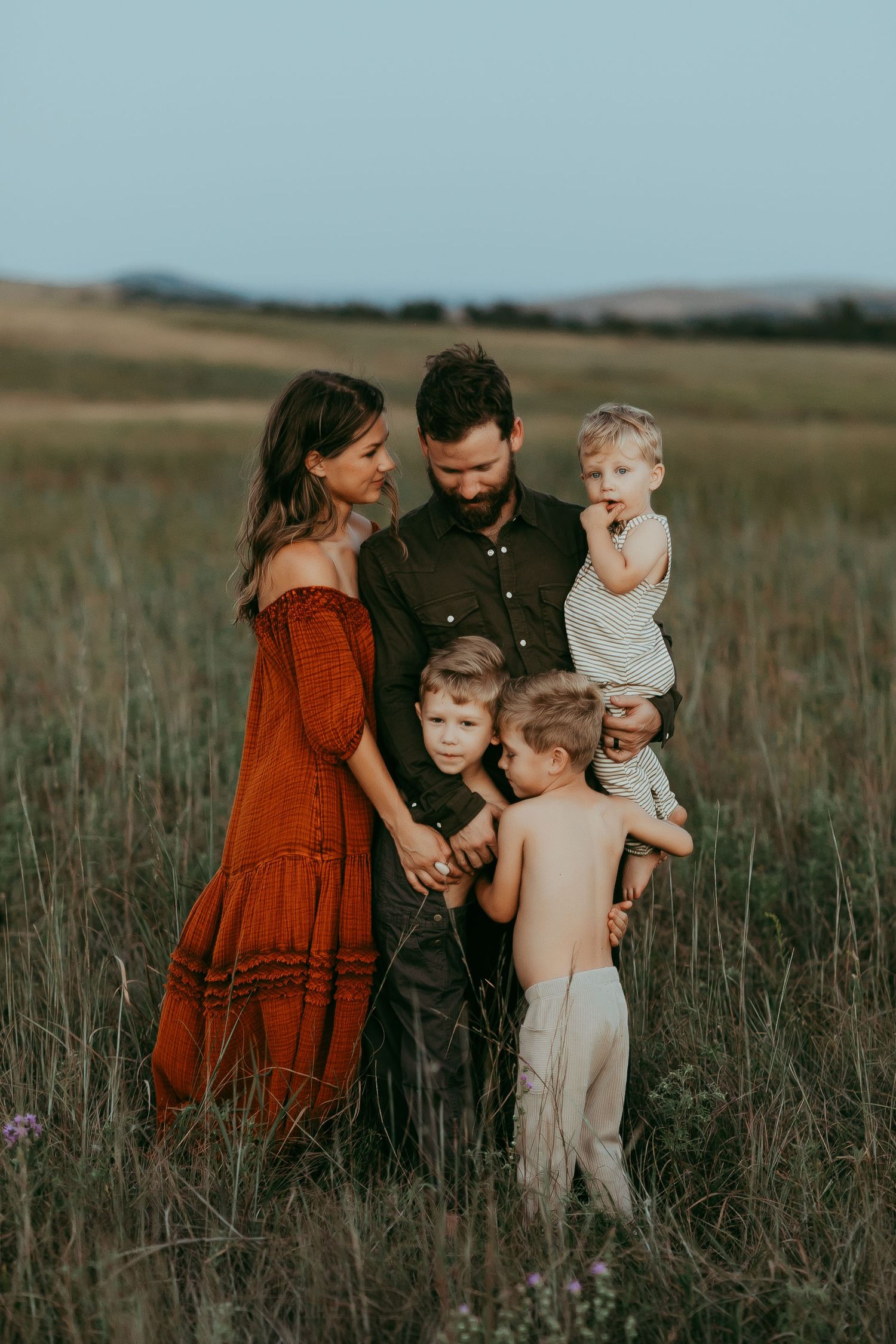 Family gathering in a rustic field during sunset with tall grass and mountains in background.