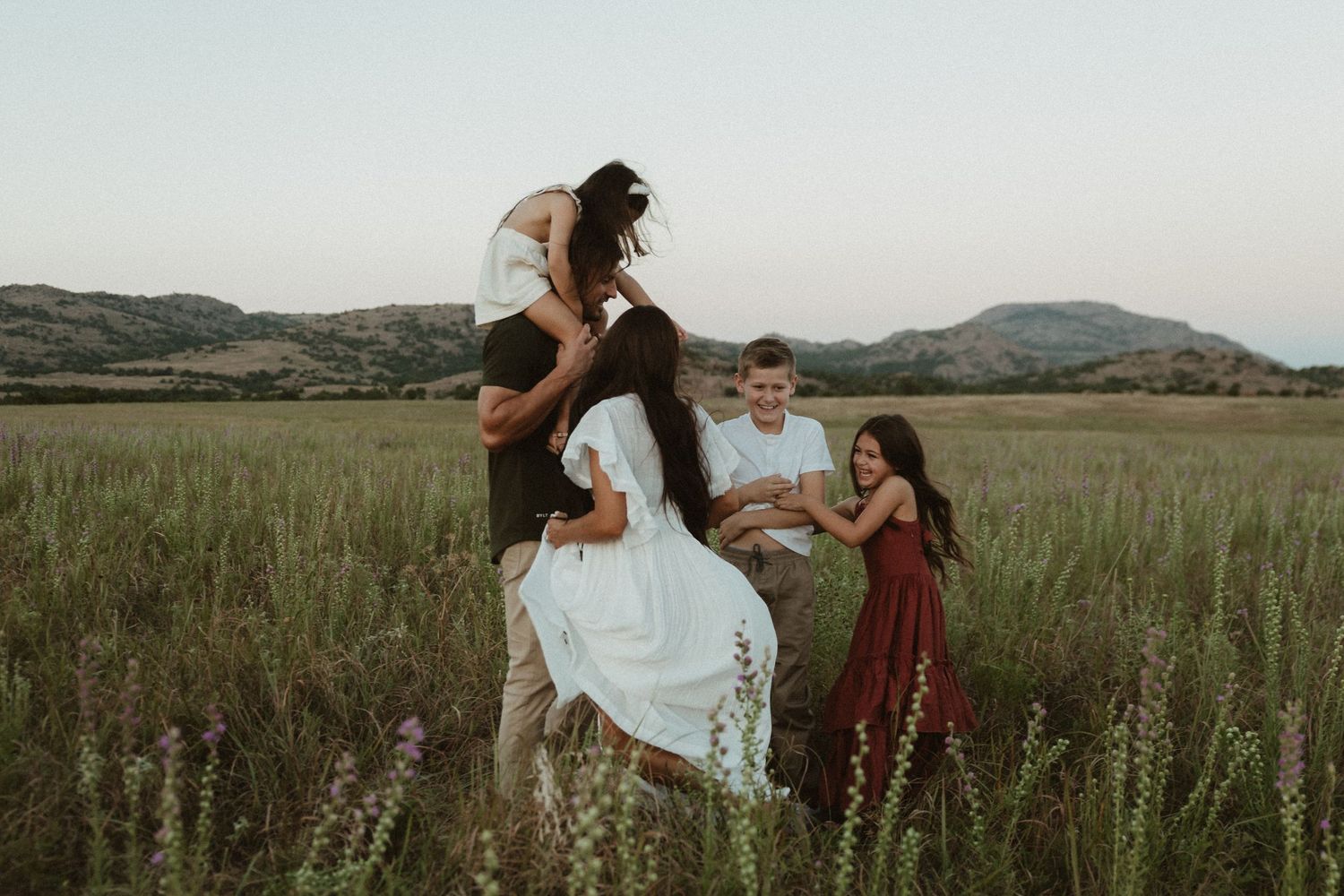People running and playing together through a tall grass field at sunset.